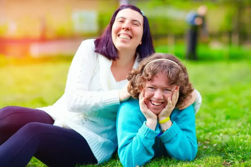 Two People Laugh While Sitting in a Grassy Park — CQ Home Care in Yeppoon, QLD