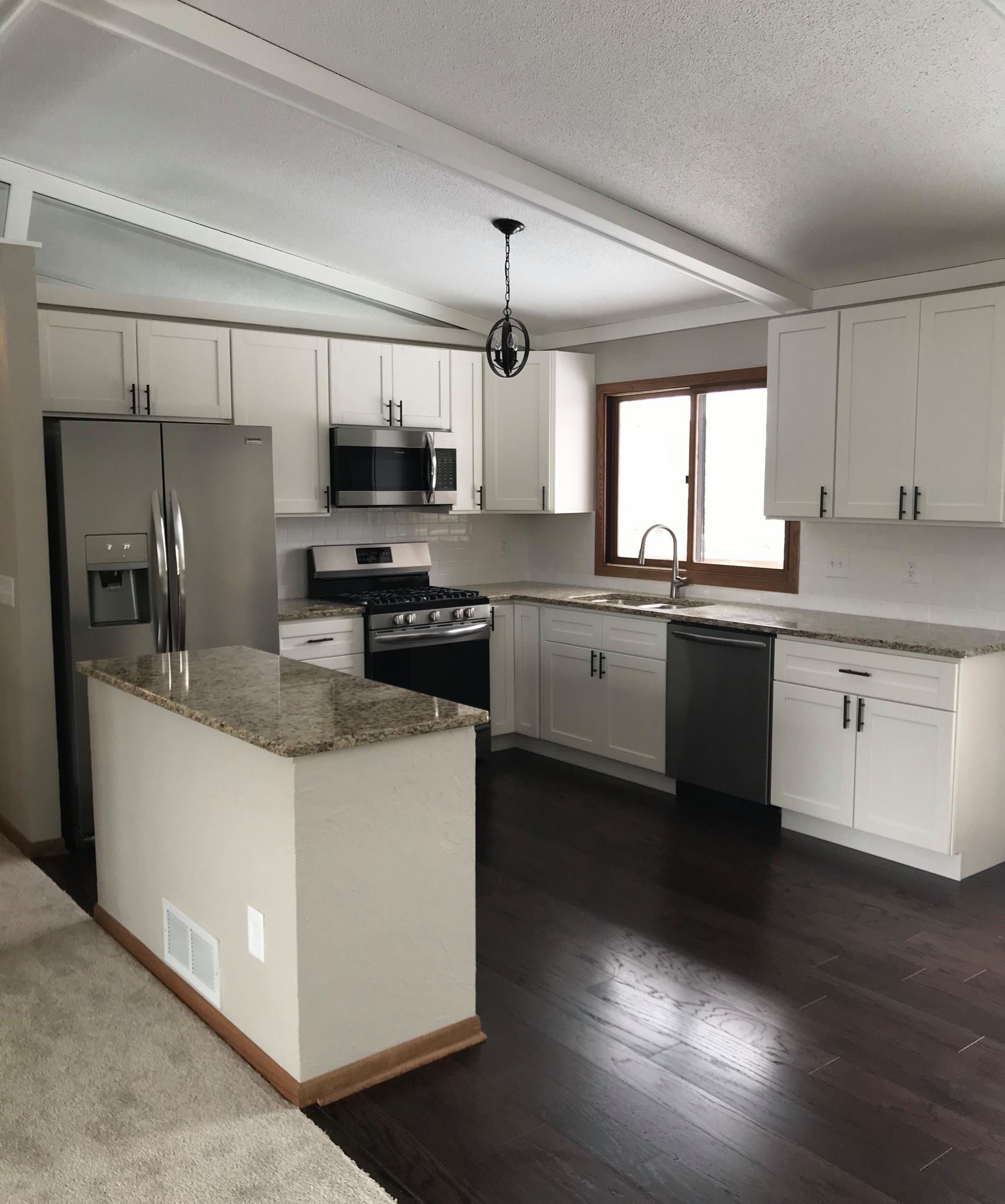 White kitchen with granite countertops, stainless steel appliances, and dark wood floors.