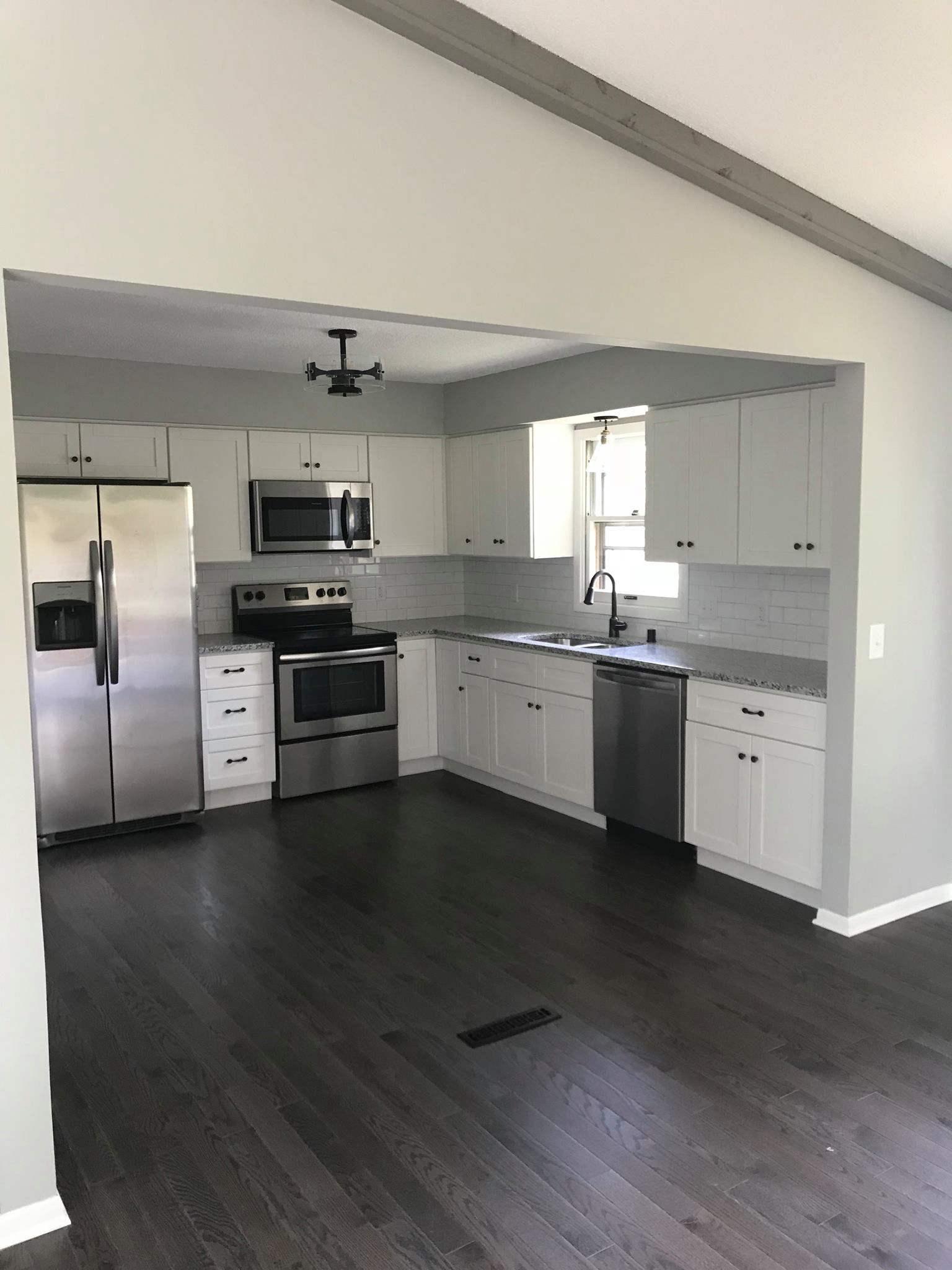 Modern kitchen with white cabinets, stainless steel appliances, gray countertops, and dark wood floors.