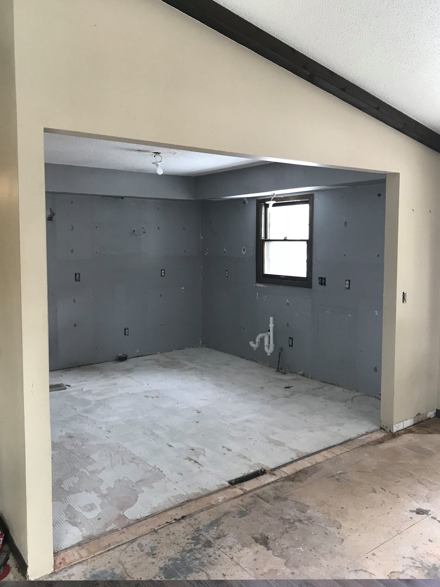 Empty room undergoing renovation; gray walls, exposed floor, window, beige trim.