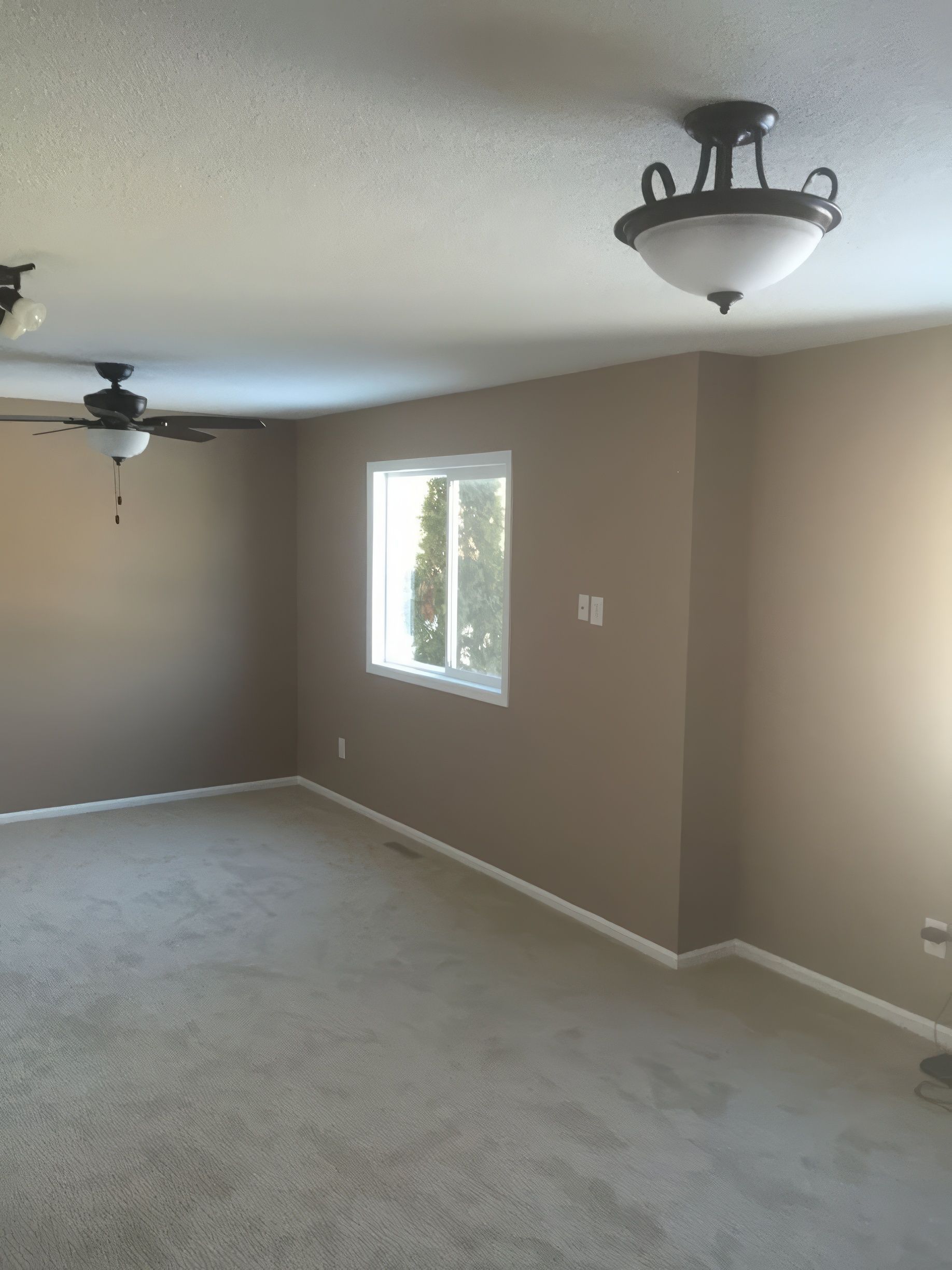 Empty room with beige walls, white window, tan carpet, and ceiling lights.