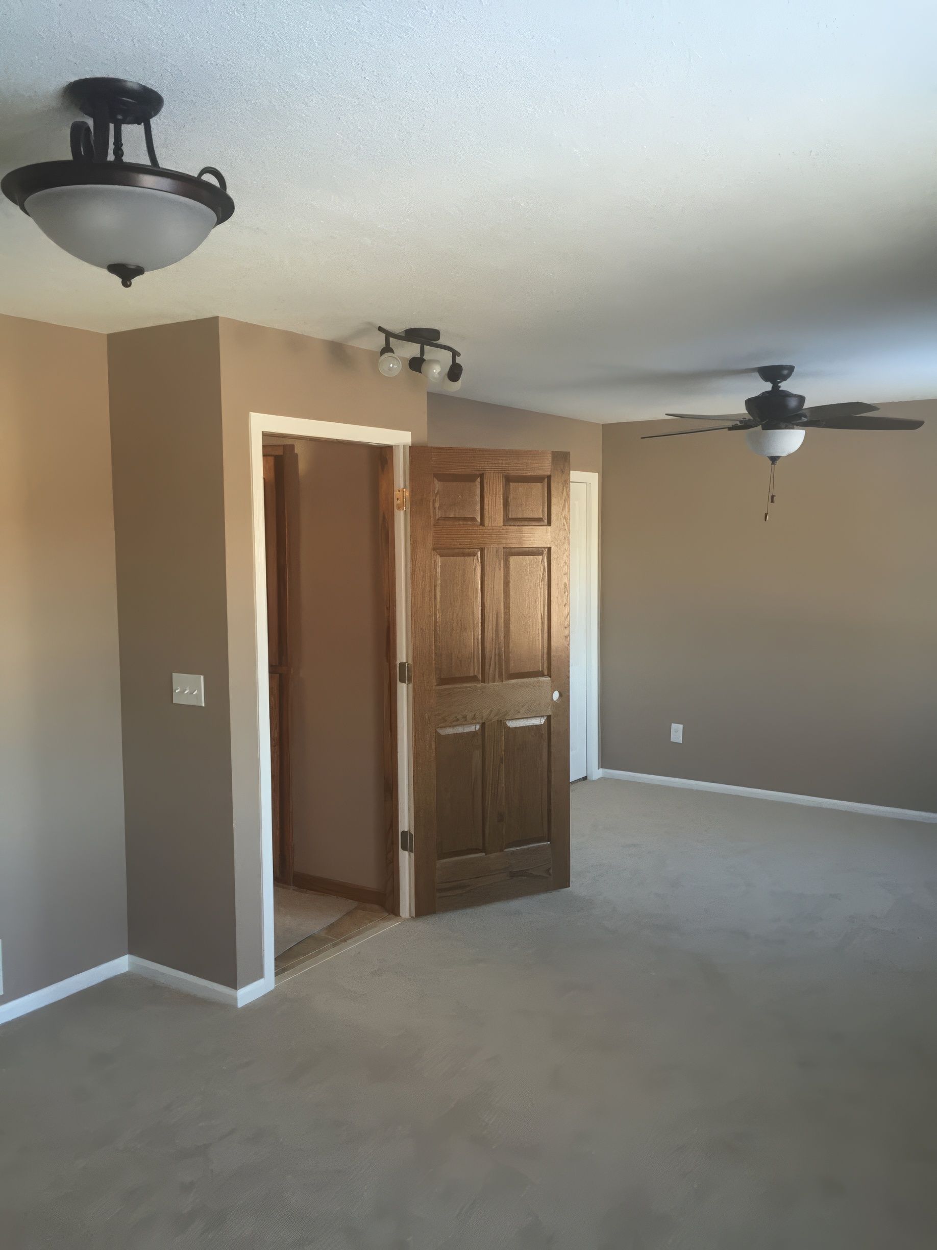 Bedroom with tan walls, carpet, ceiling fans, and a brown wooden door leading to another room.