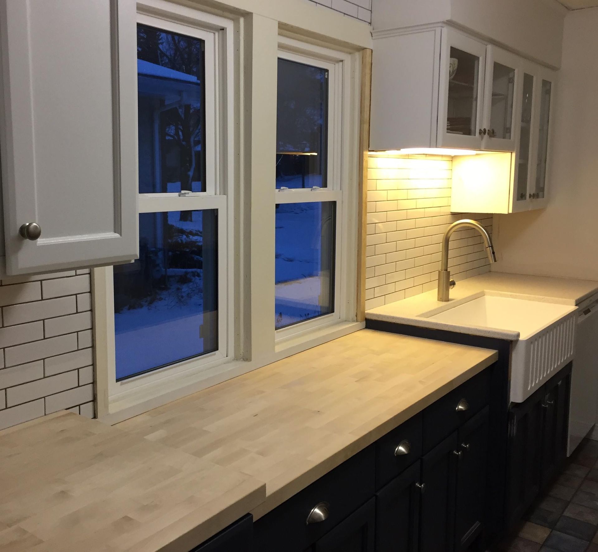 Kitchen with light wood countertops, white subway tile backsplash, dark blue cabinets, and a white sink.