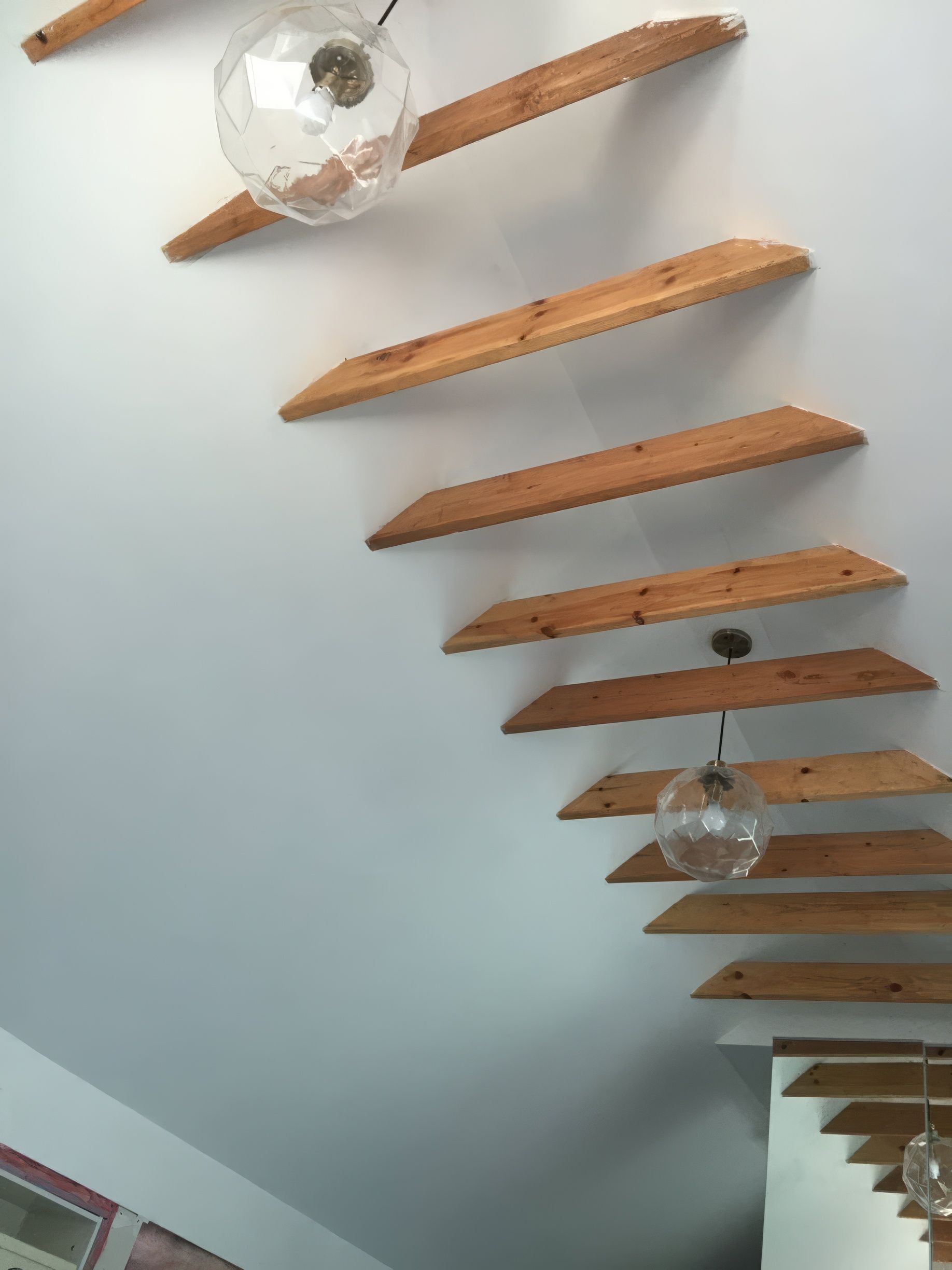 Floating wooden staircase with globe lights against a white wall.