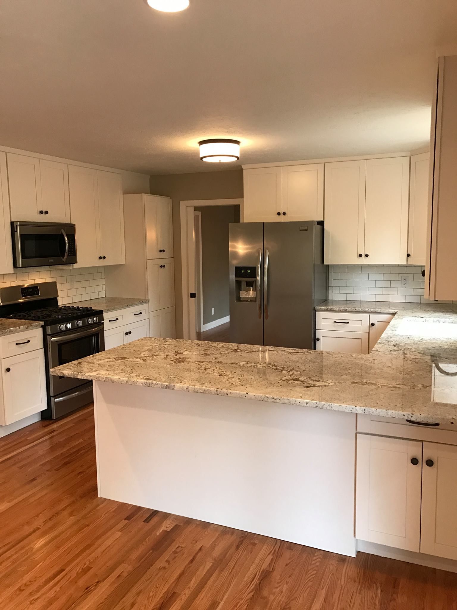 White kitchen with island, stainless steel appliances, and wood floors.