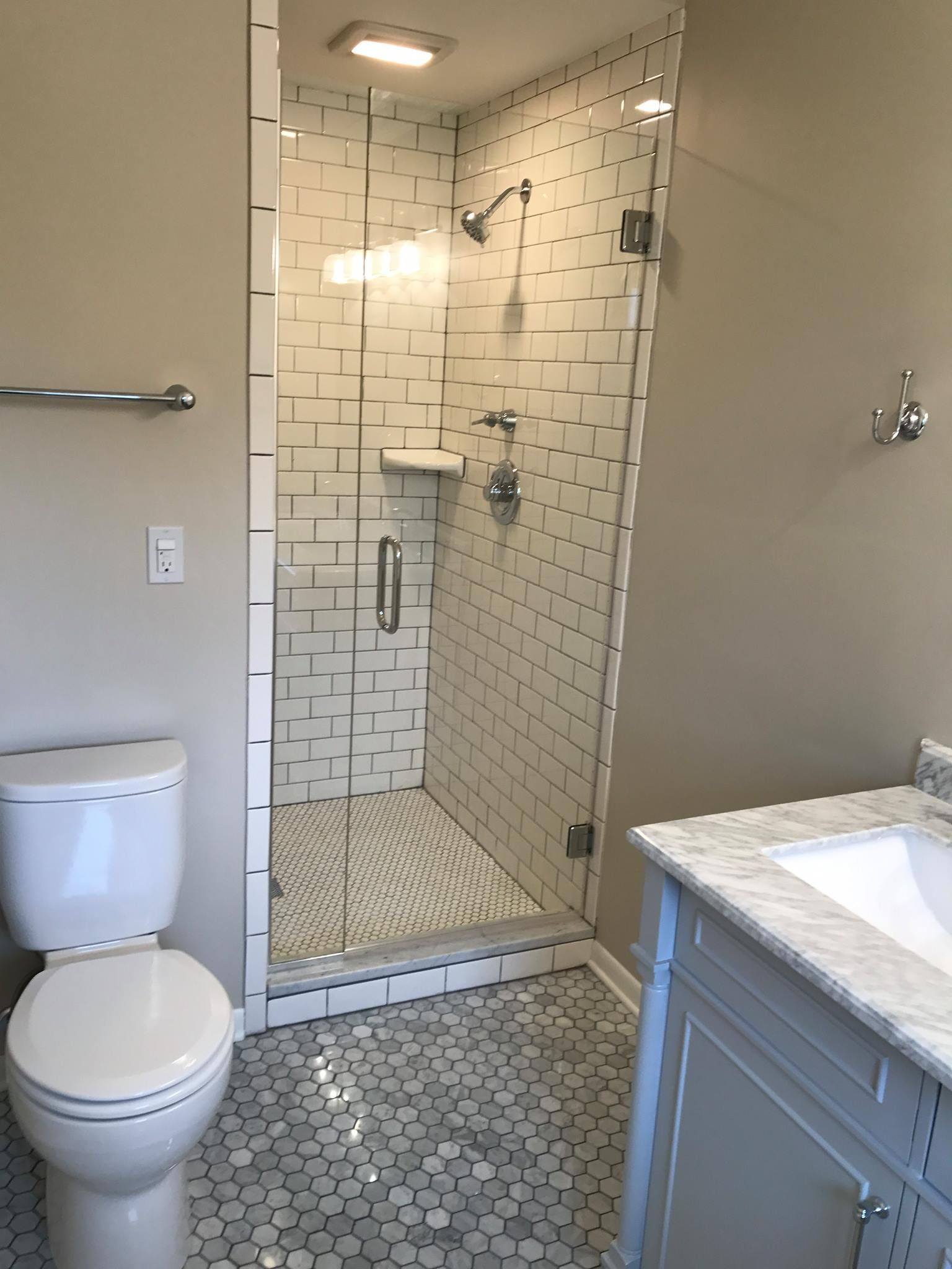 Bathroom with a white toilet, sink, and glass shower with mosaic tile flooring and walls.