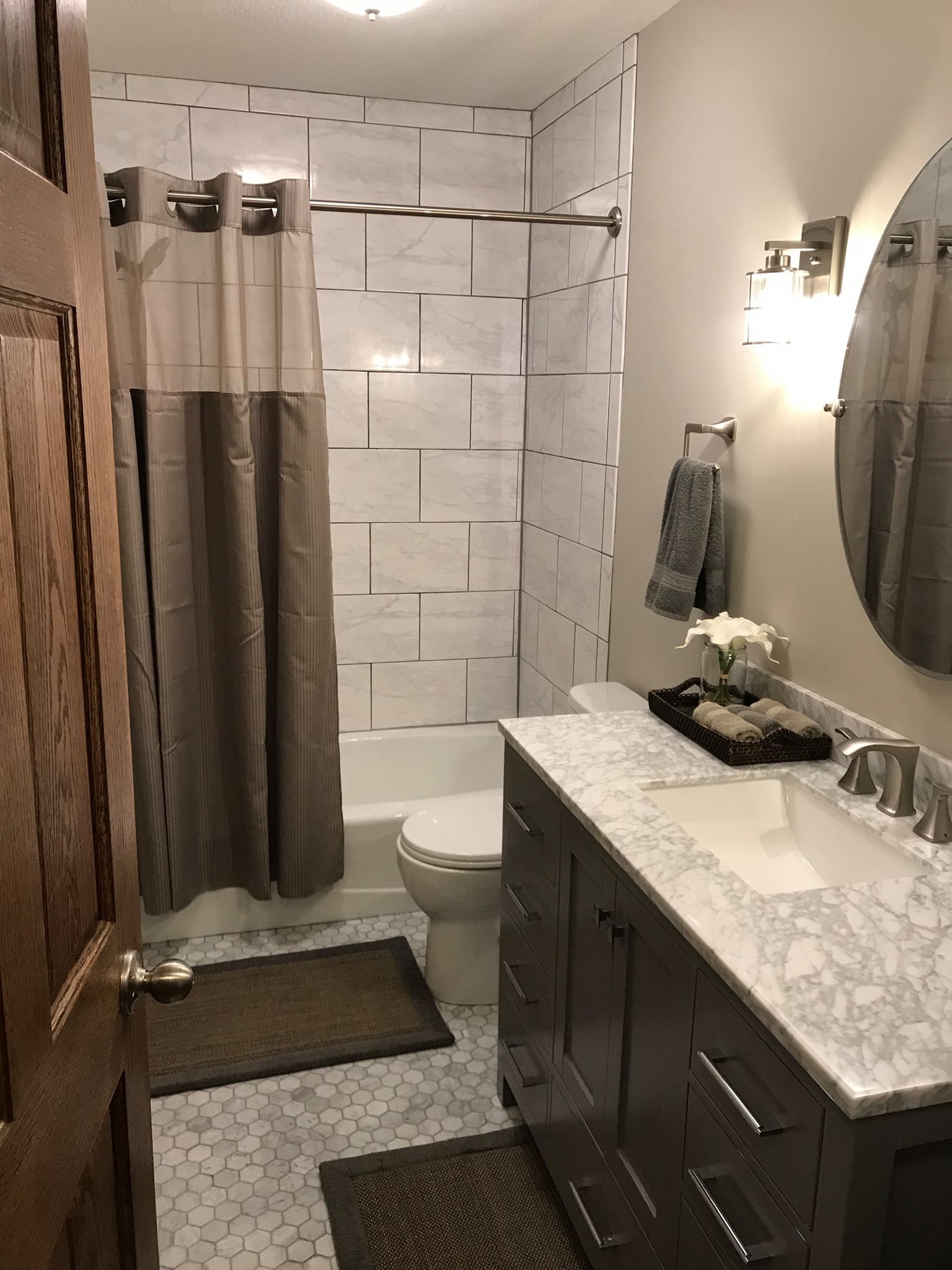 Bathroom with shower, vanity, toilet. Brown door and accents, white and gray tile, and neutral colors.