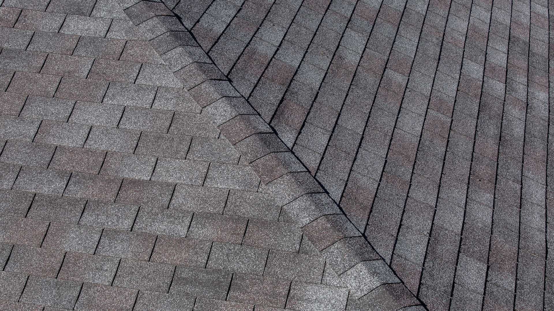 Close-up of asphalt shingle roof sections, varying shades of gray, joined at an angle.