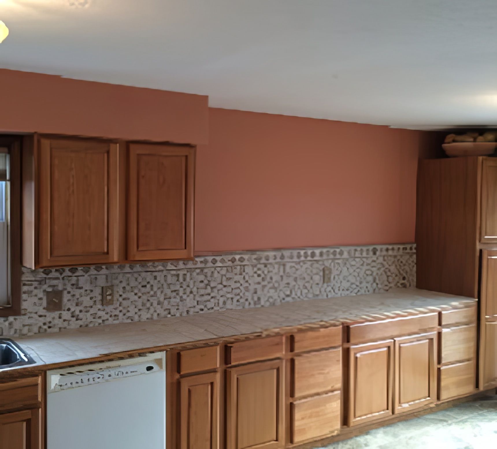 Kitchen with wooden cabinets, white appliances, coral wall, and tiled backsplash.