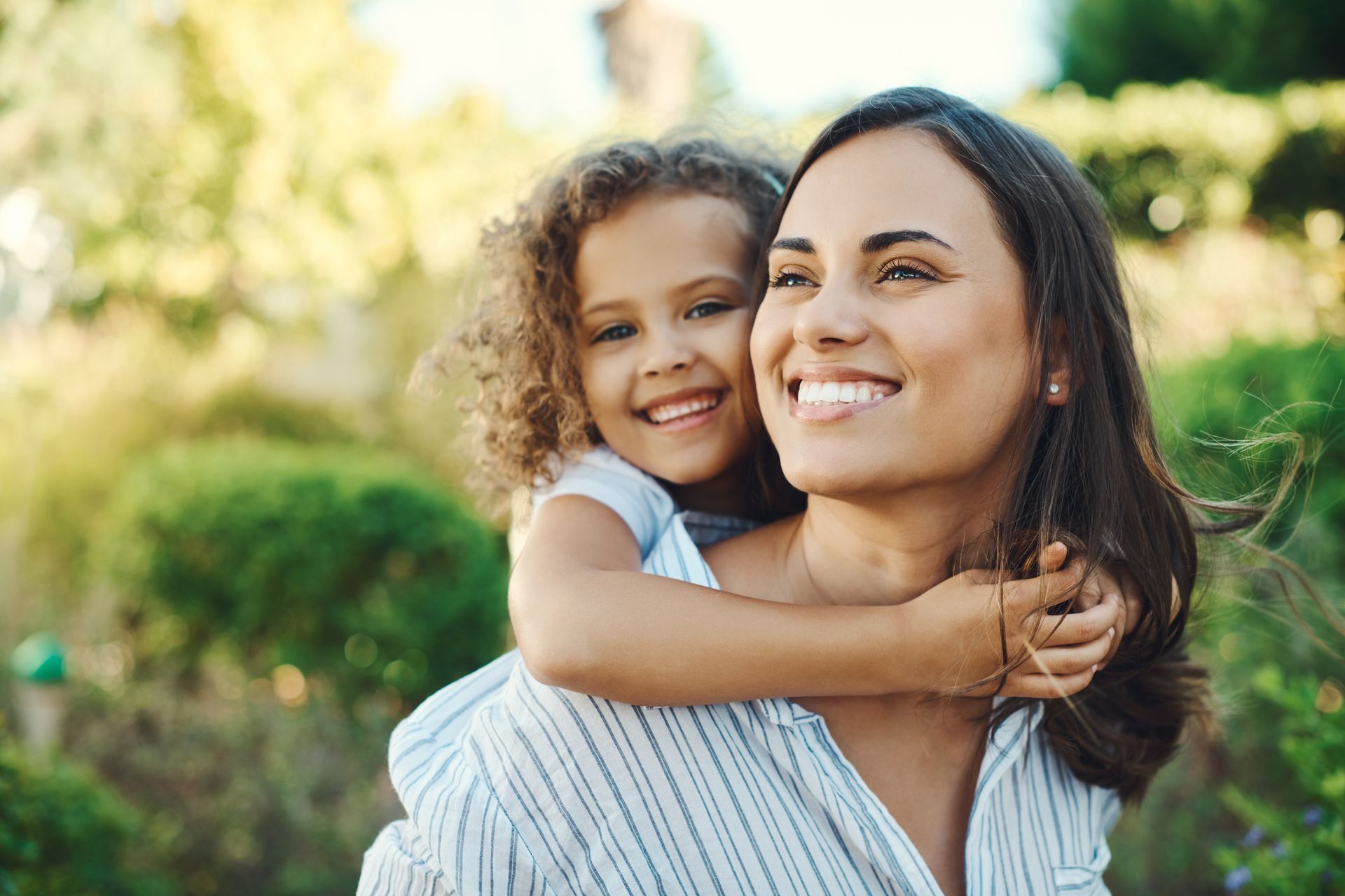 Mom with daughter on back at a park.