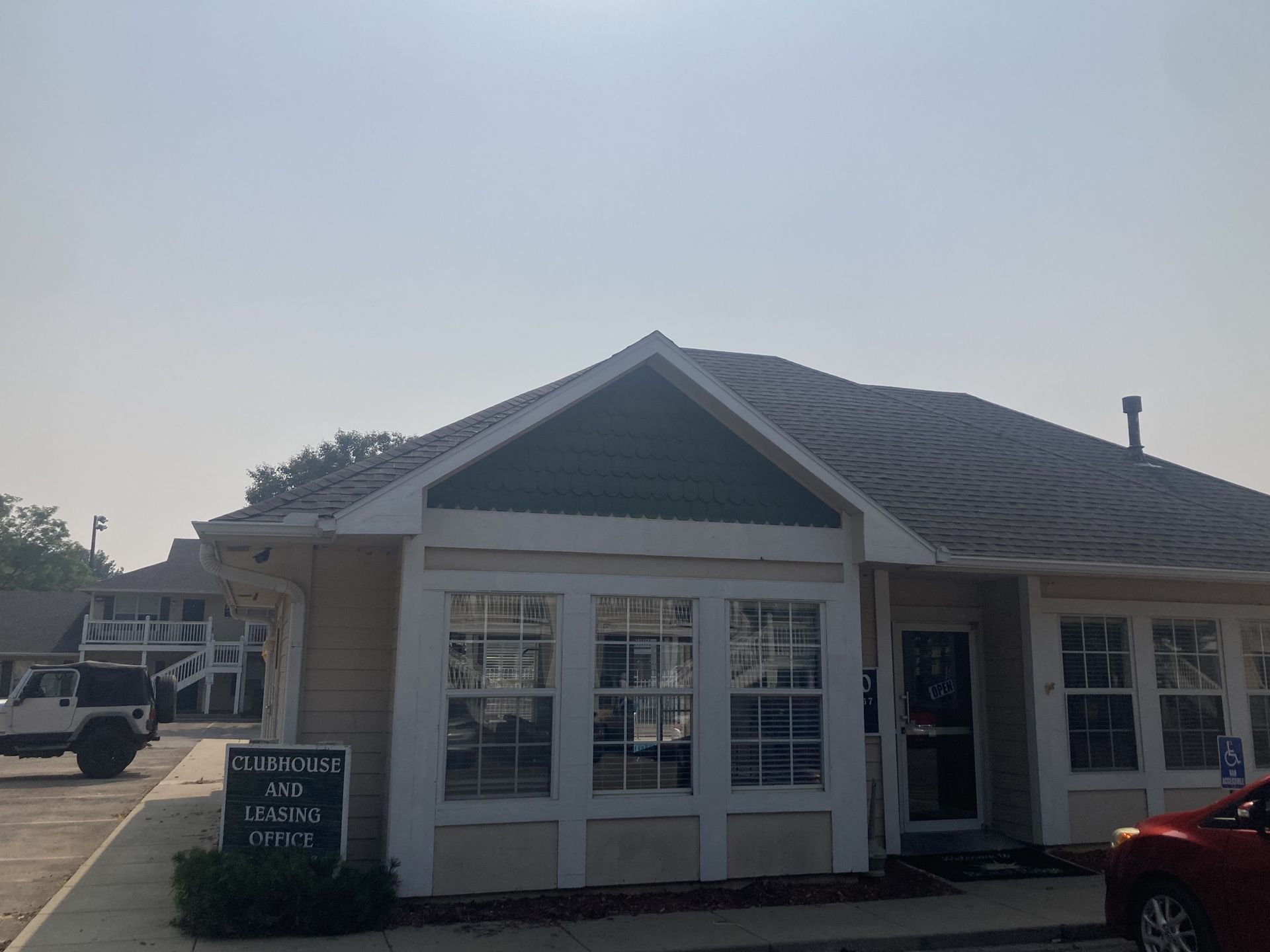 Exterior of a building with windows, a sign, and a car in front. Overcast sky.