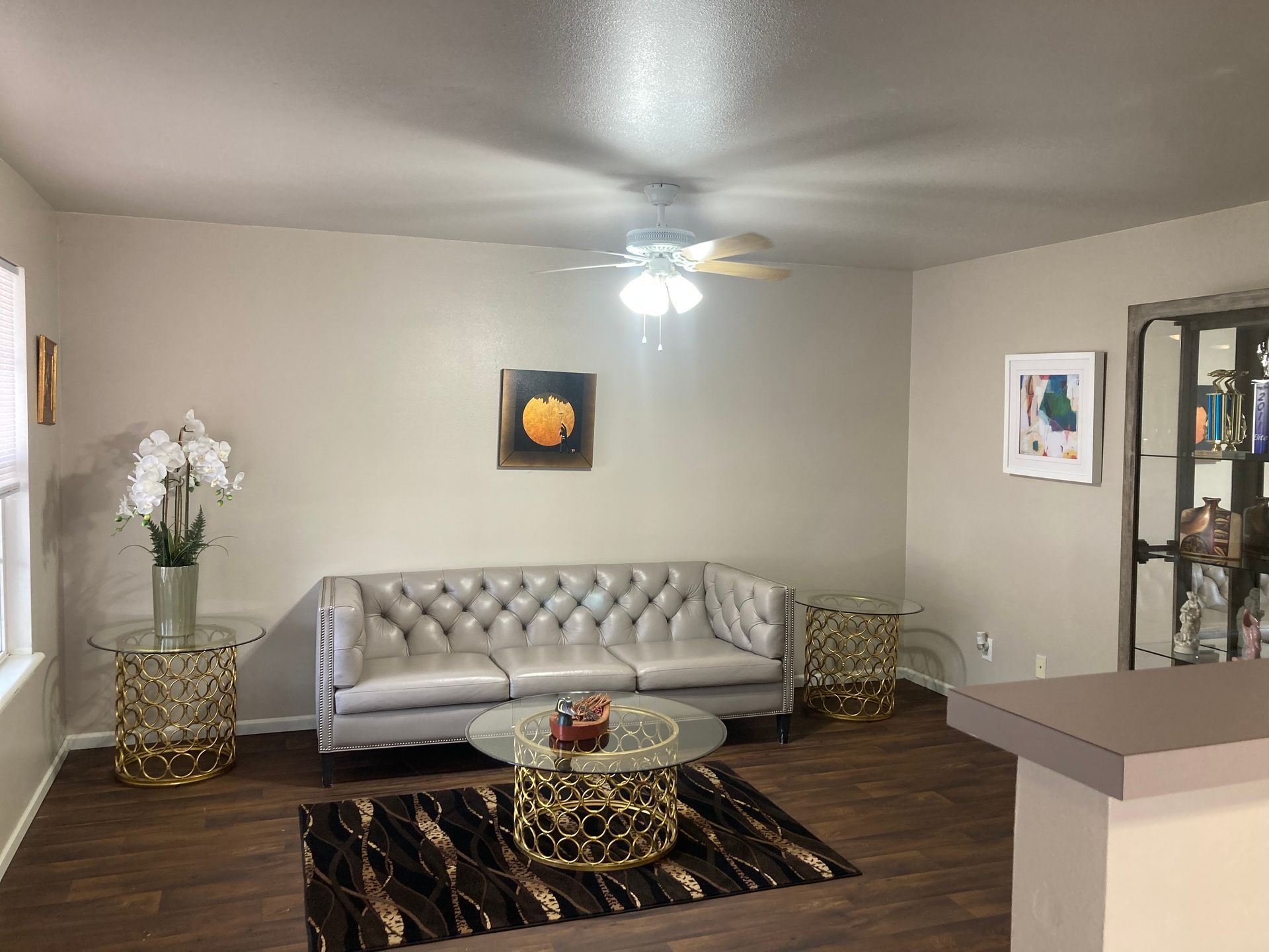 Living room with a silver couch, gold accents, and artwork on the walls.