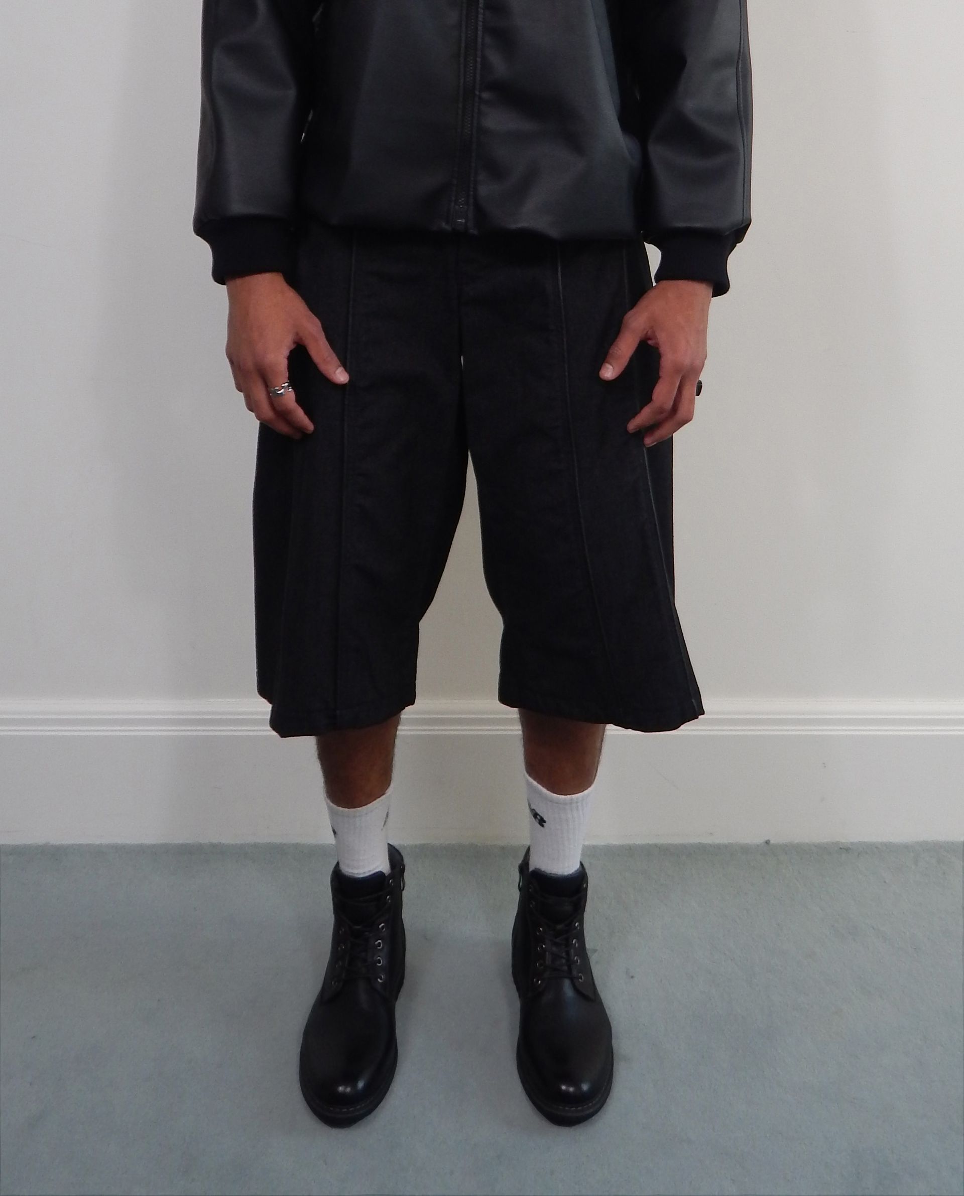 Person wearing black jacket, shorts, white socks, and boots, standing in front of a wall.