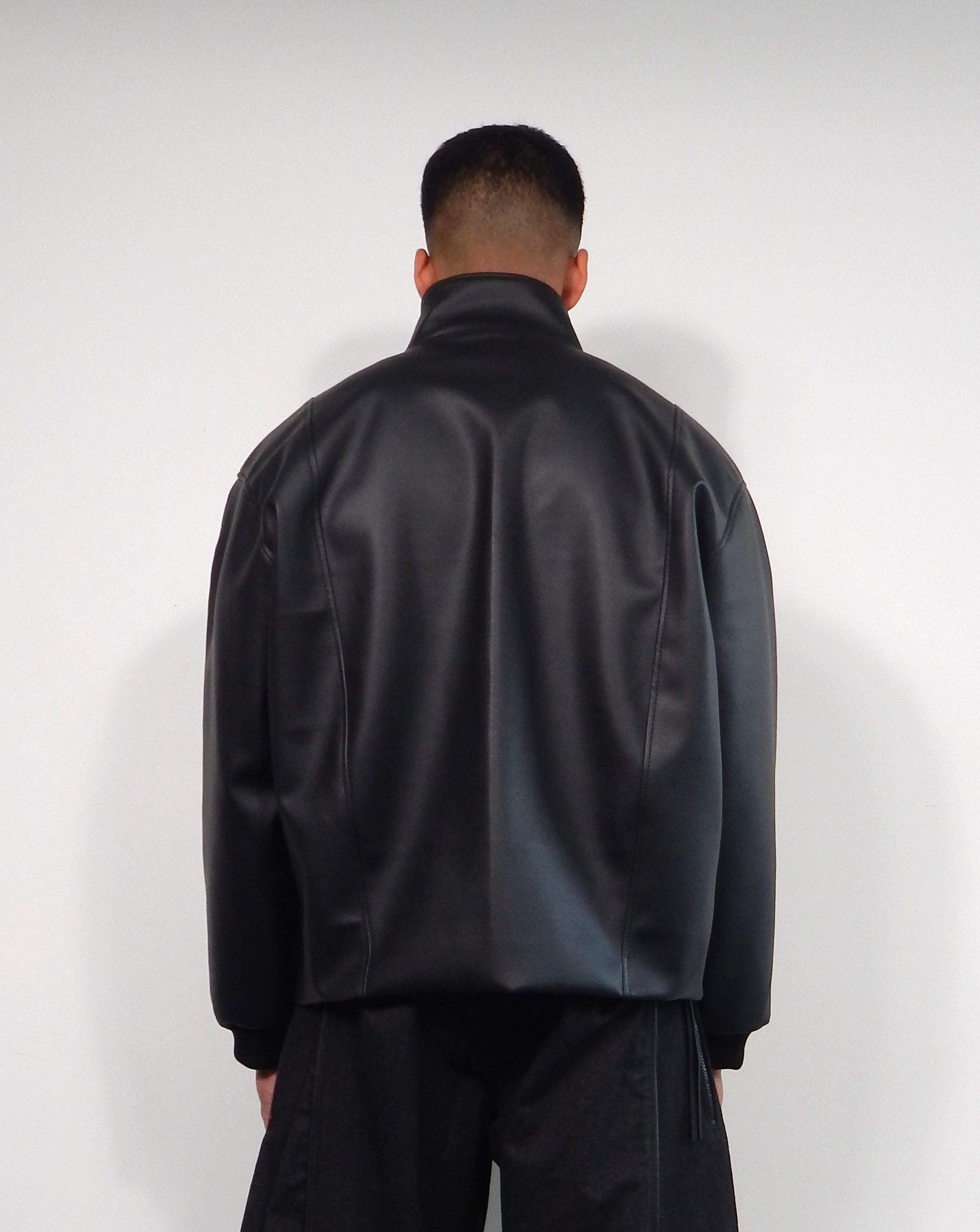 Man wearing a black bomber jacket, viewed from the back, against a white background.