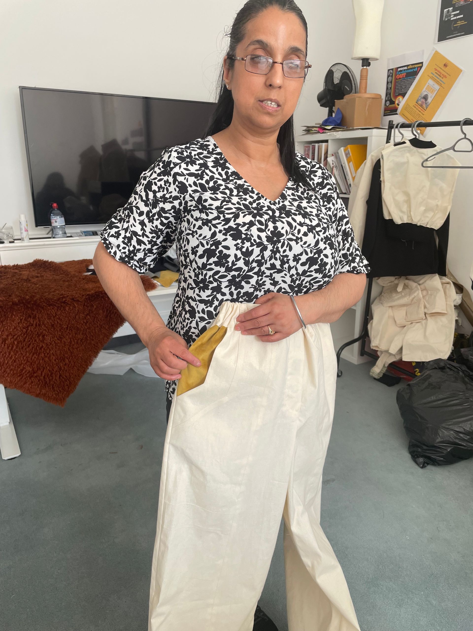 Man in off-white jacket with hand in pocket, red-tinted glasses, in a classroom setting.