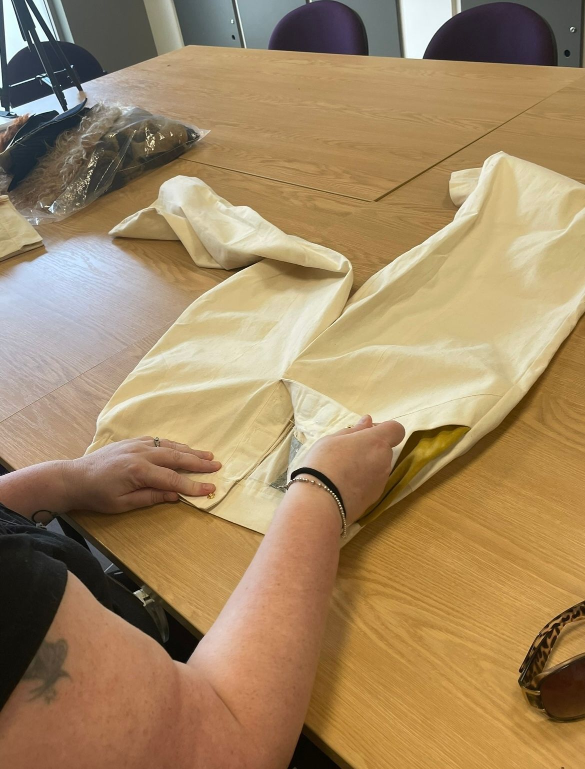Person folding a pair of cream-colored pants on a wooden table.