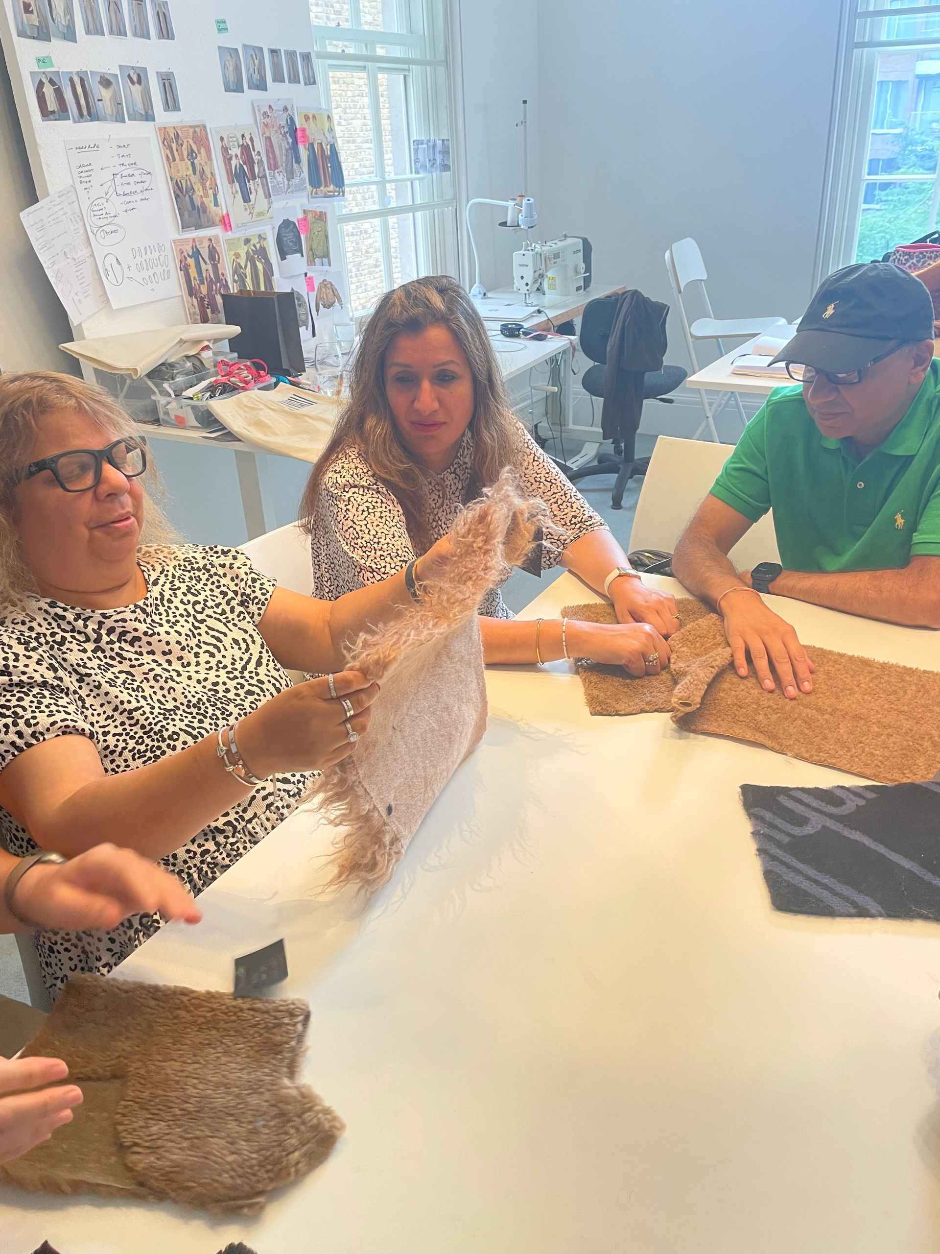 Three people examining fabric swatches at a table in a well-lit workshop.