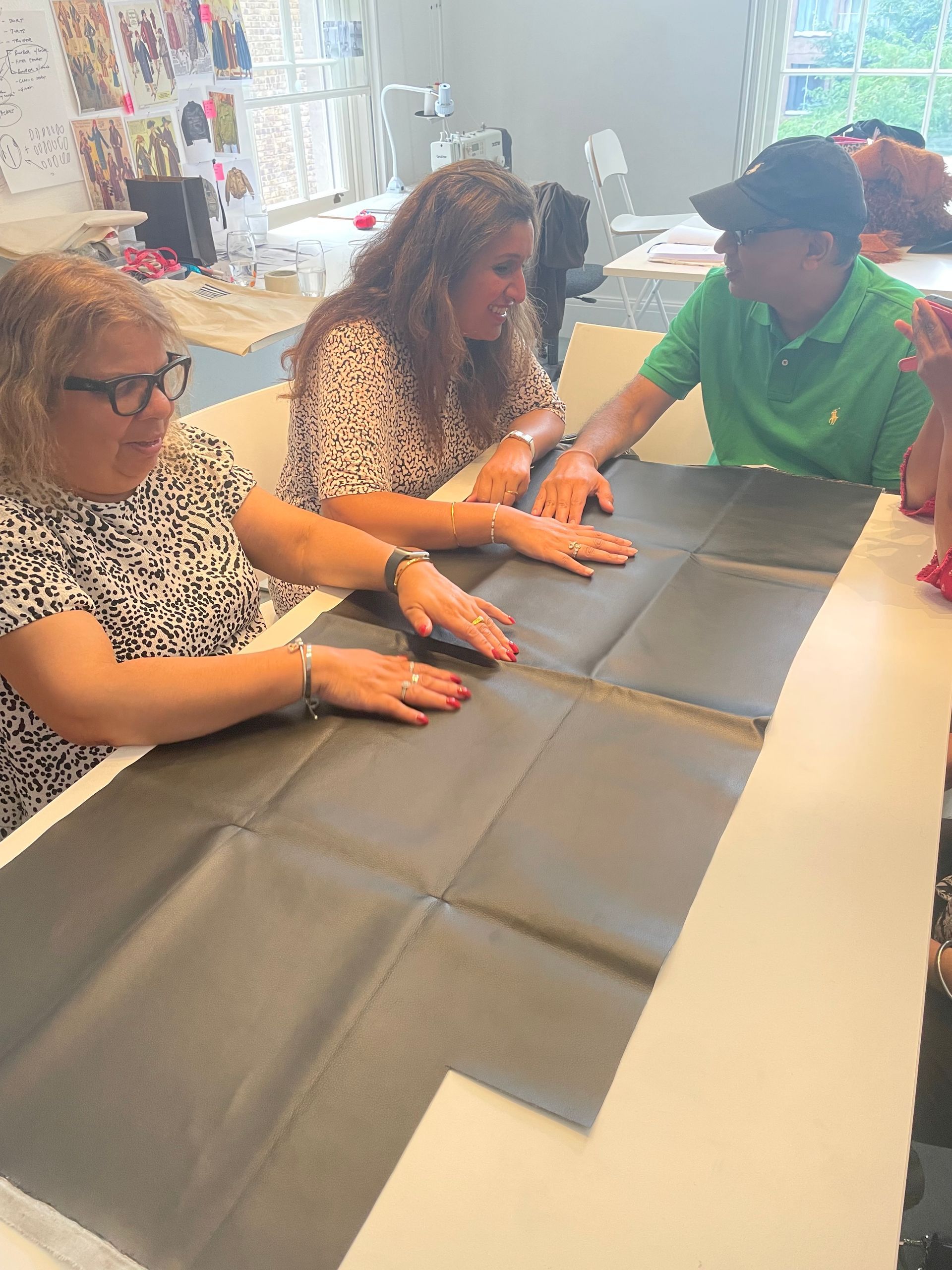 Three people touching a large, folded black piece of leatherette on a white table. They're in a brightly lit room.