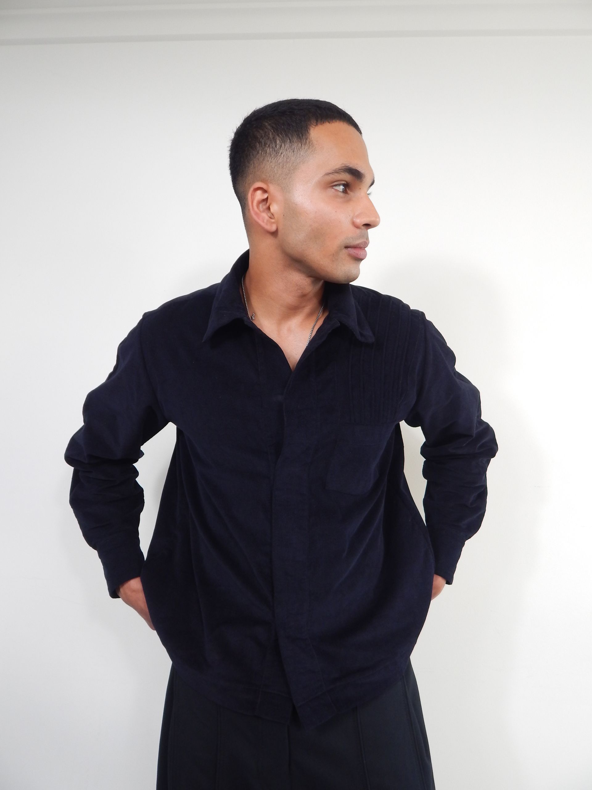 Man in dark blue shirt, hands in pockets, looking to the side, against a white background.