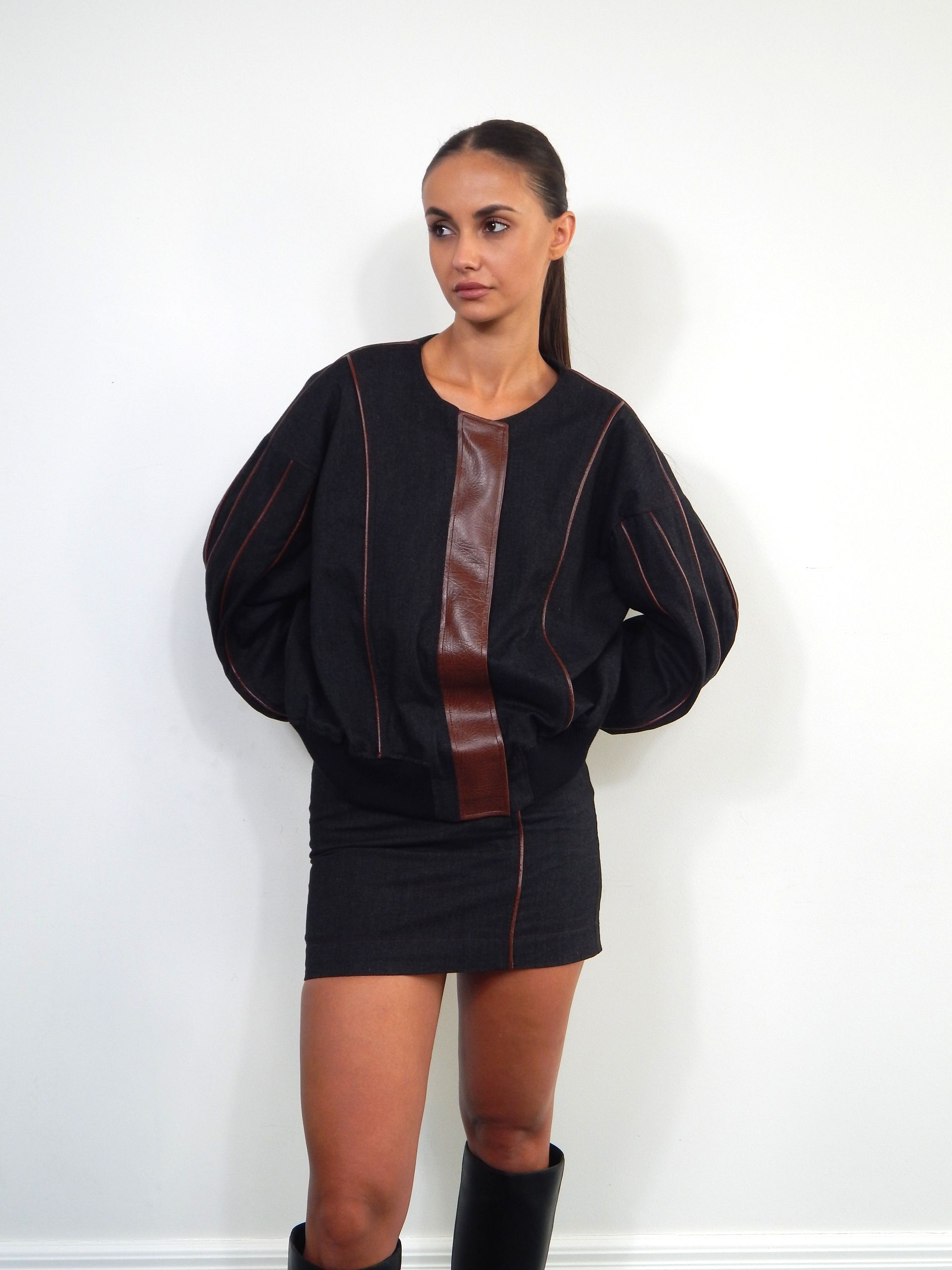 Woman in black outfit, brown leather panel, standing, looking to the side.