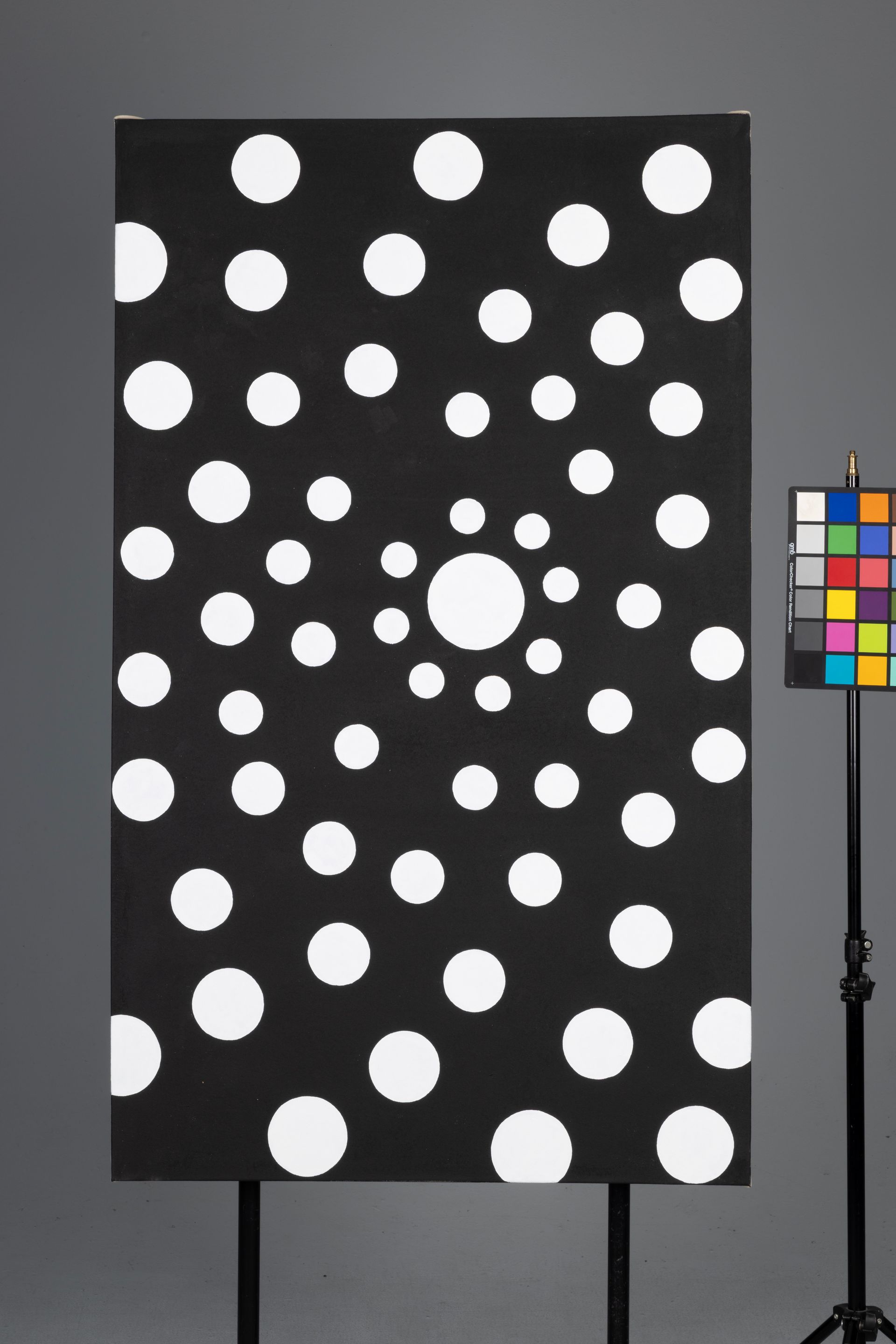 Black panel with white polka dots beside a color calibration chart on a stand