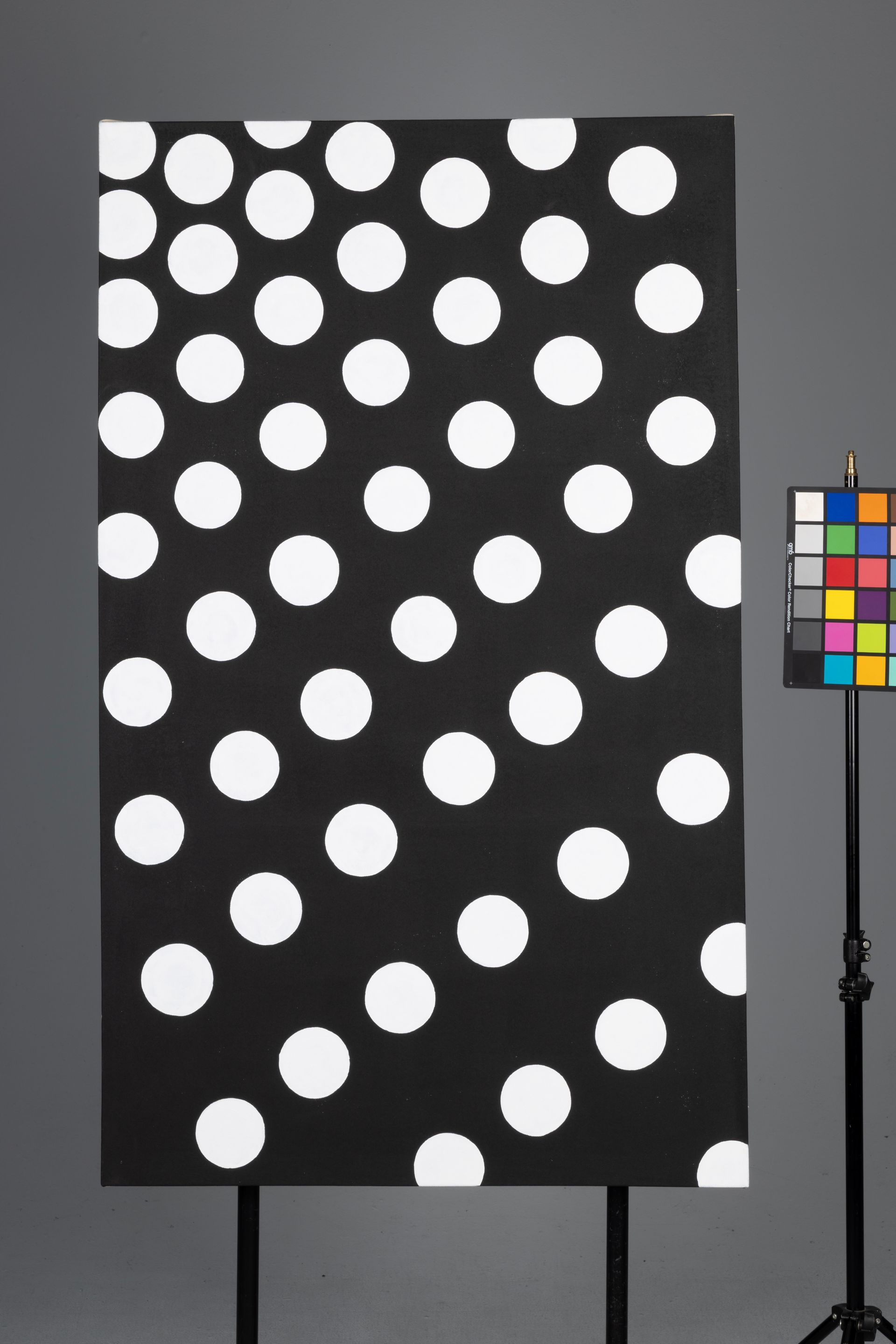 Black panel with many white polka dots beside a color calibration chart on a stand.