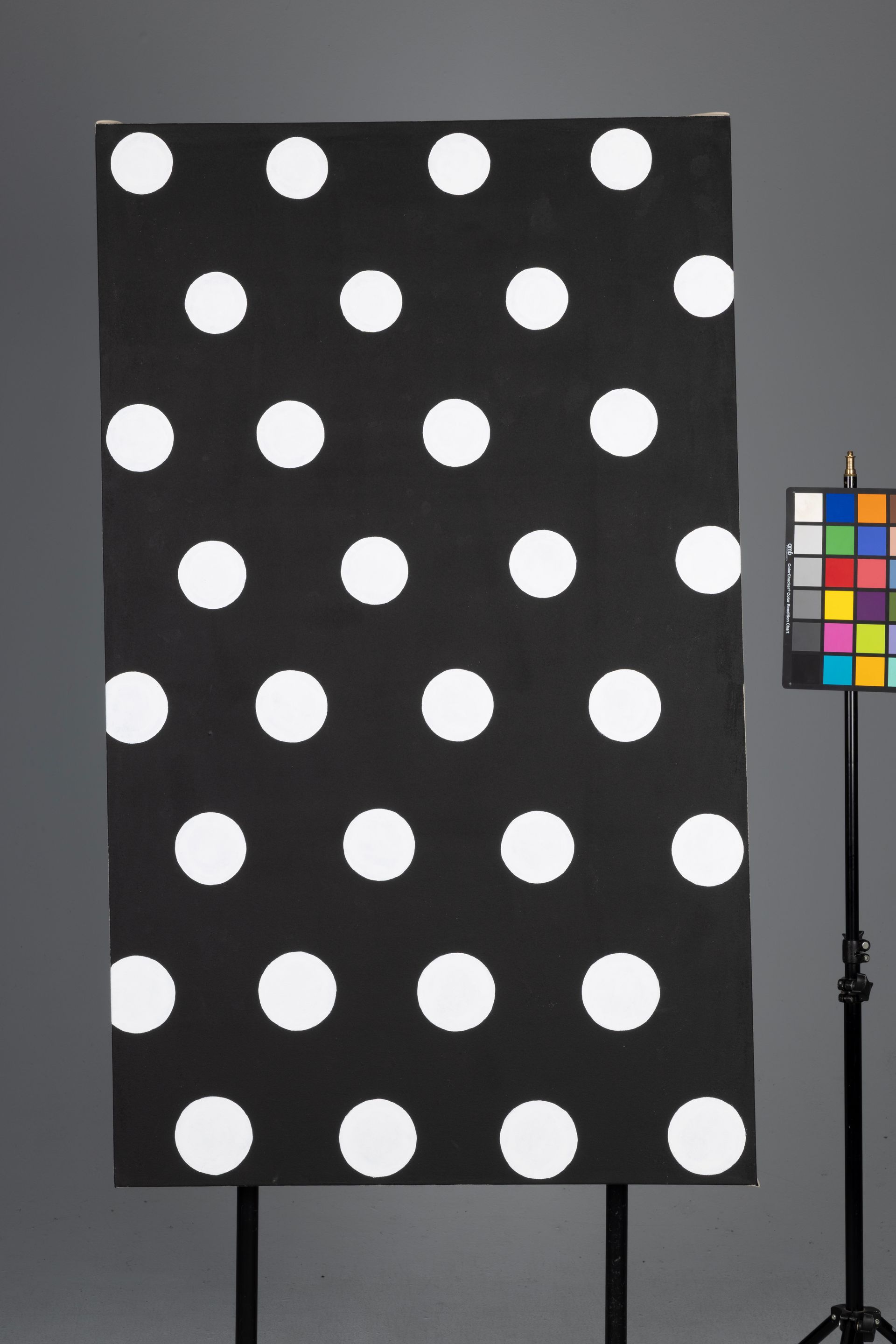 Black board with large white polka dots beside a color calibration chart on a stand.