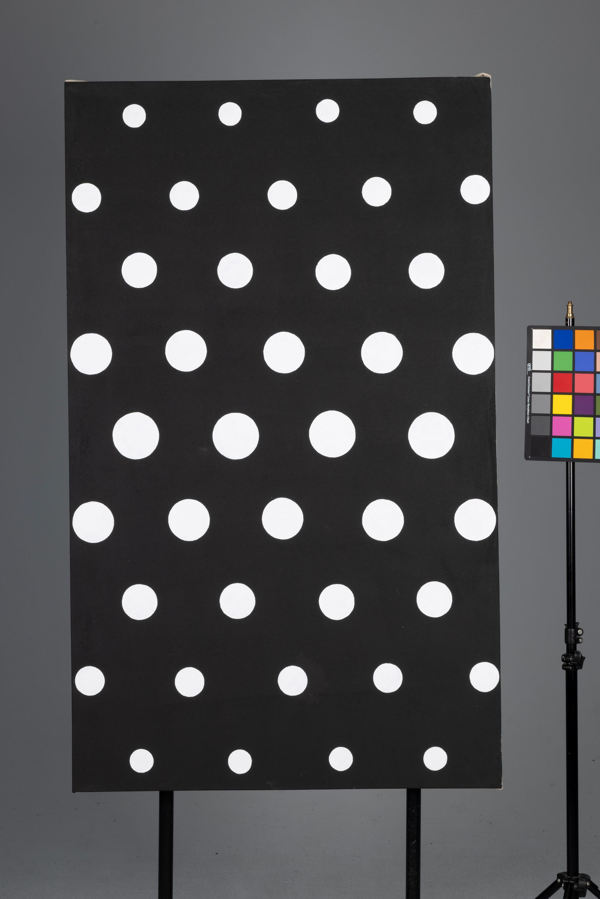 Black board with rows of white dots beside a color calibration chart on a stand.
