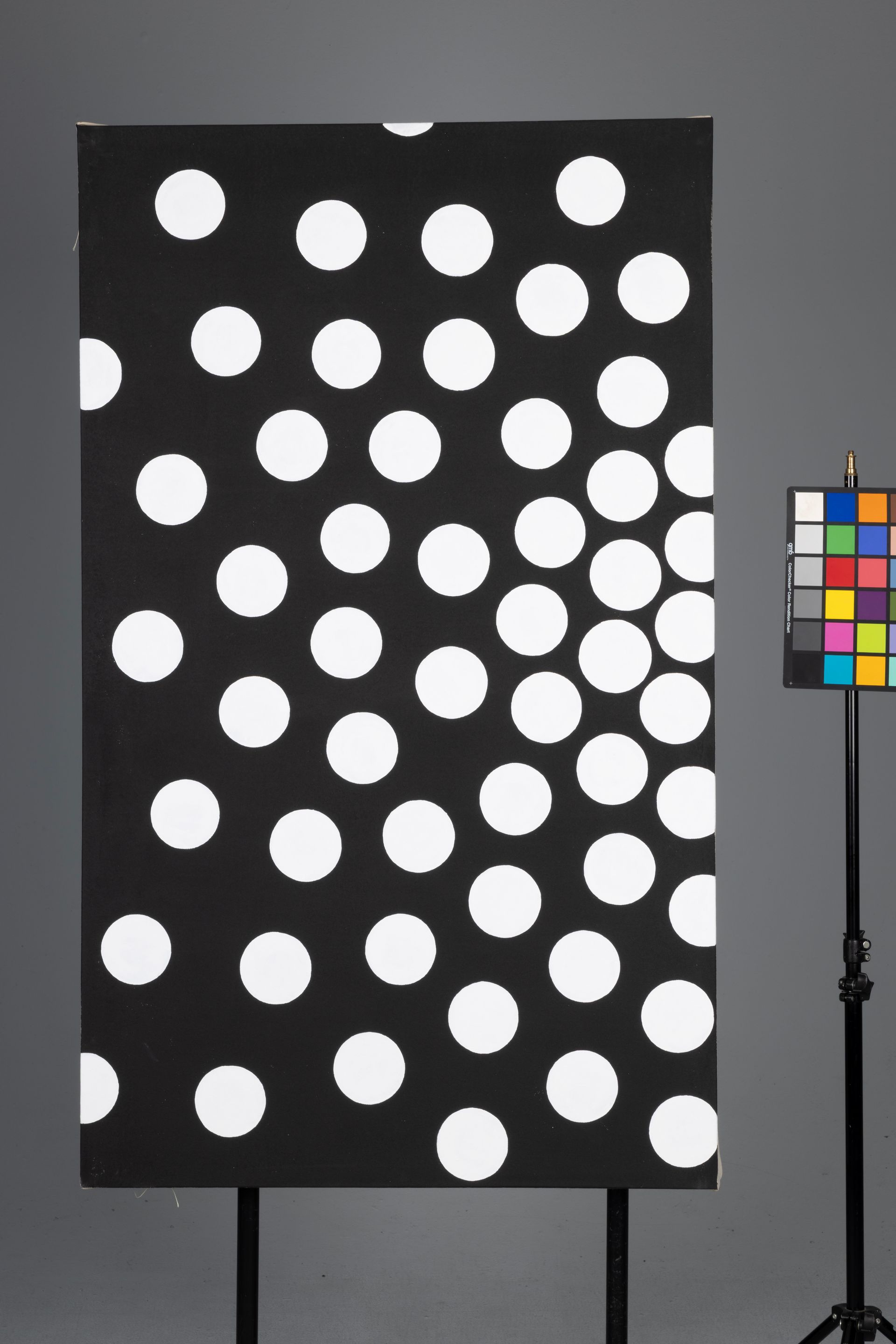 Black canvas with white polka dots beside a color calibration chart on a stand