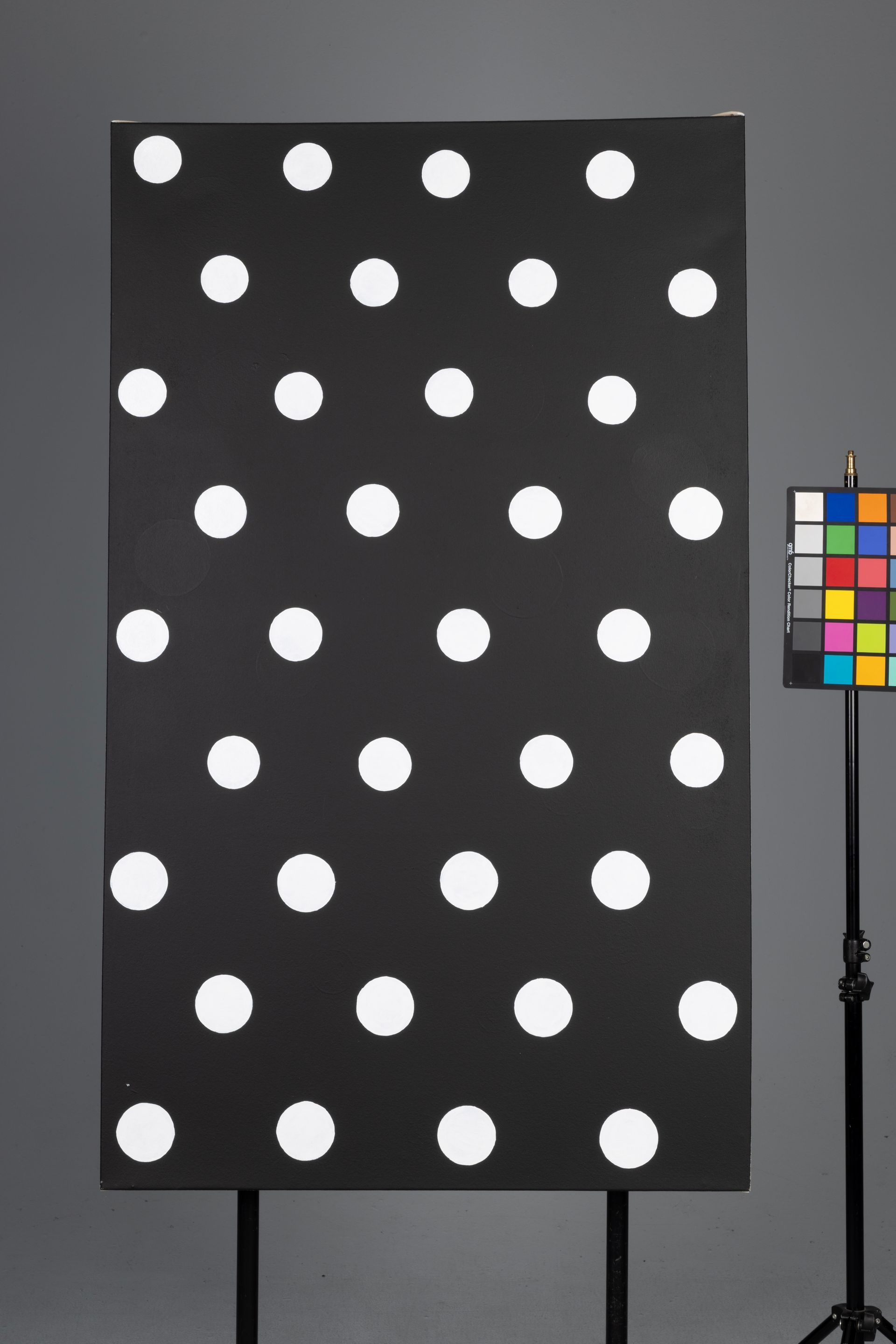 Black test chart with white polka dots beside a color calibration chart on a stand.