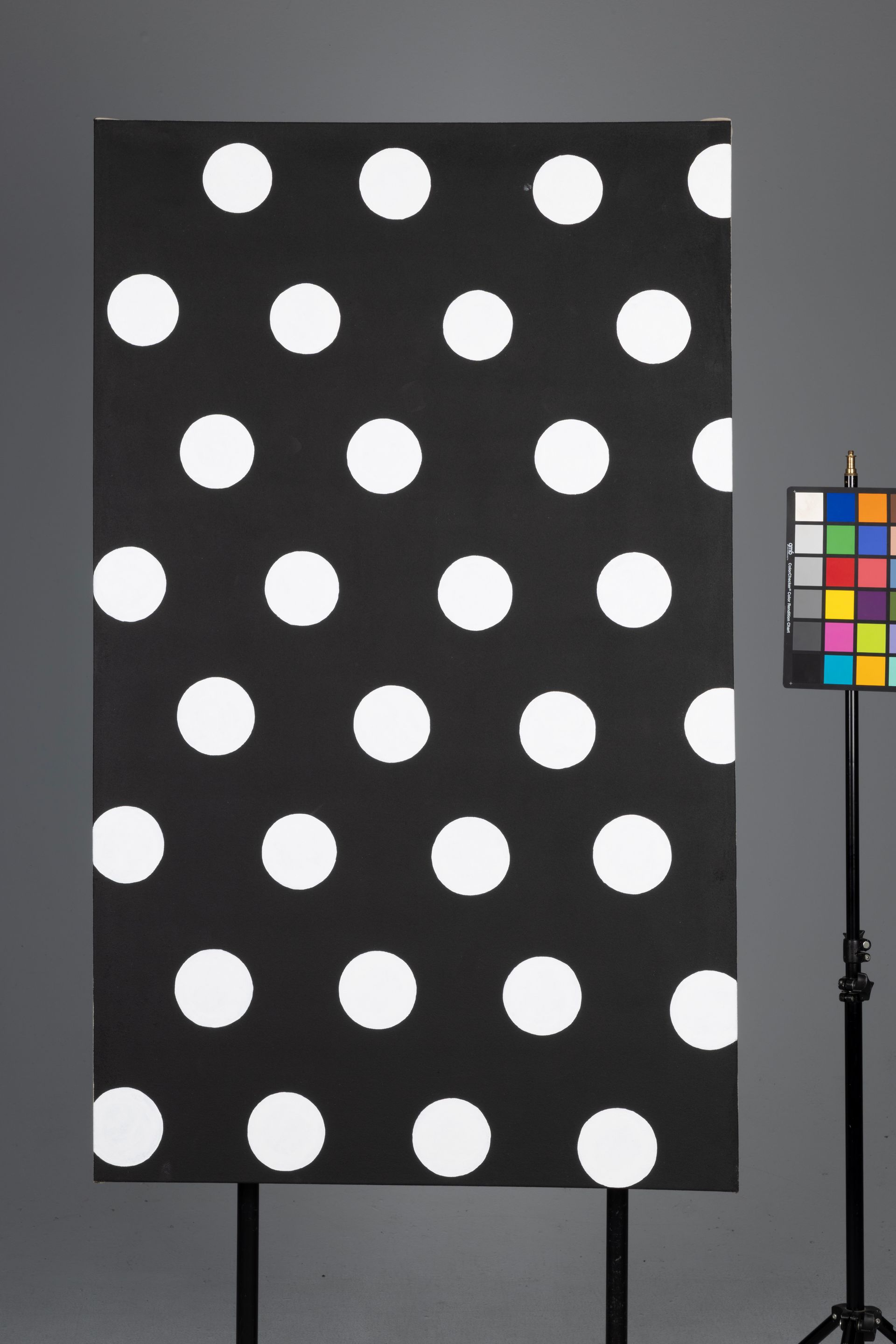 Black board with large white polka dots beside a color calibration chart on a stand.