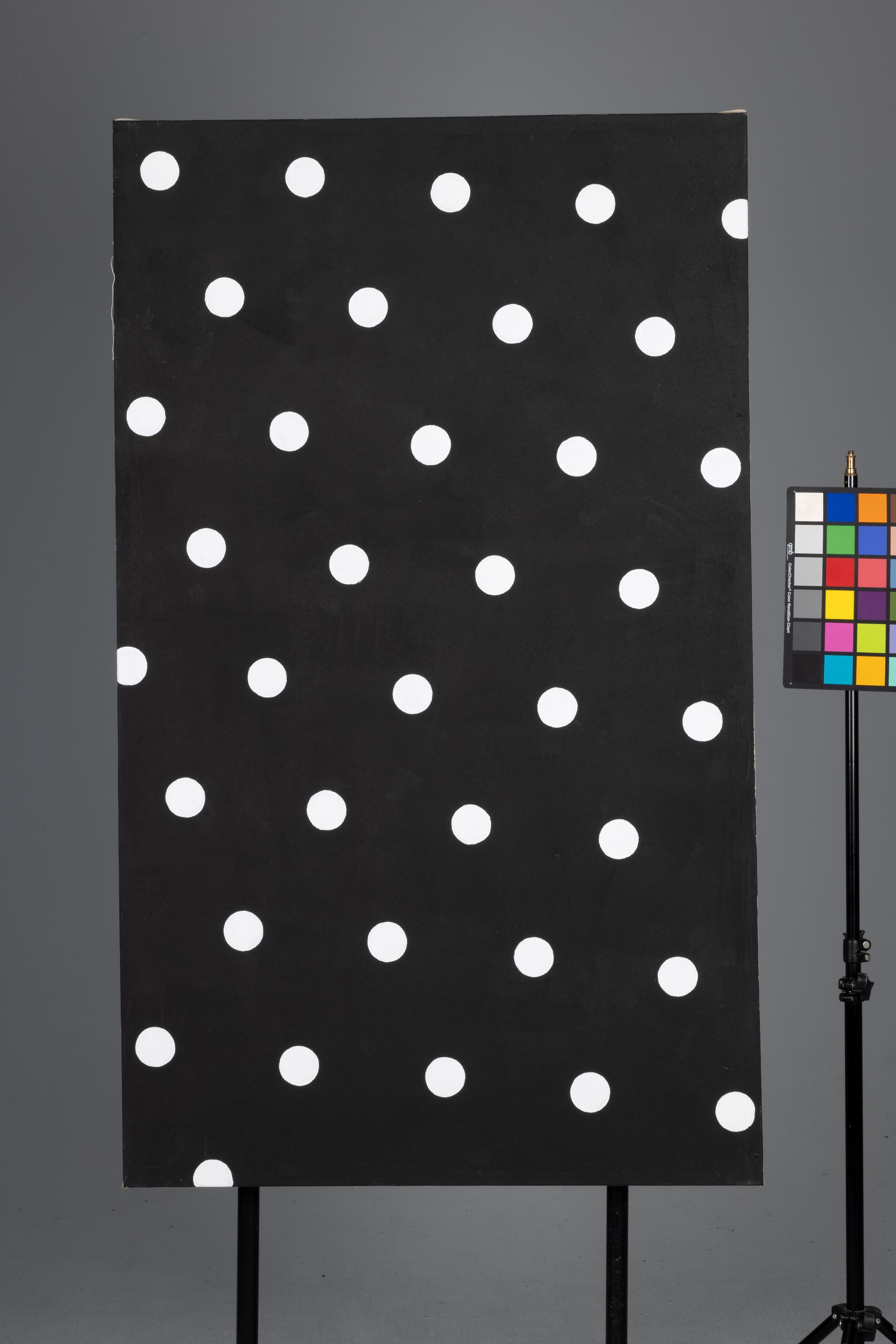 Black board with white polka dots beside a color calibration chart on a stand.