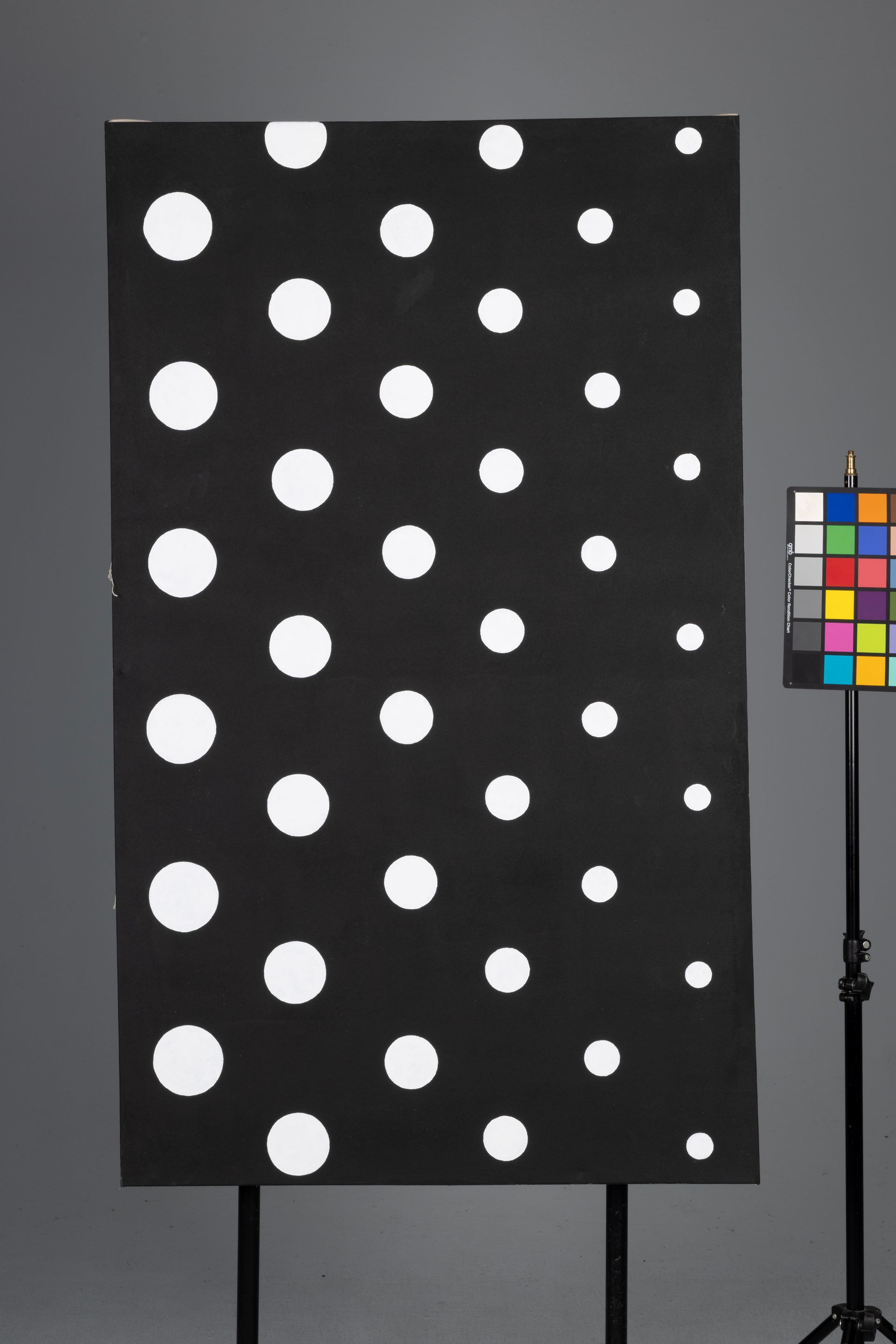 Black panel with white polka dots beside a color calibration chart on a stand