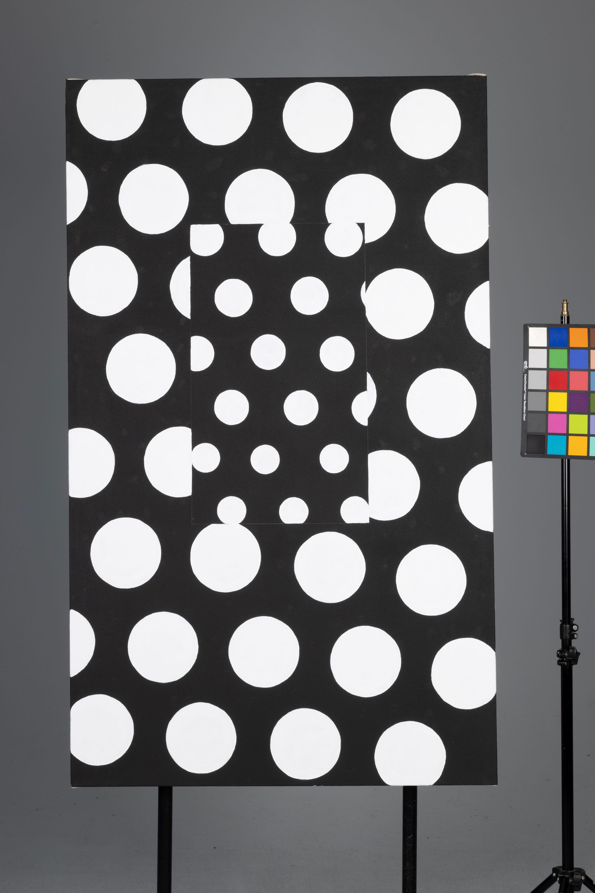 Black panel with many white circular cutouts, beside a color calibration chart on a stand.