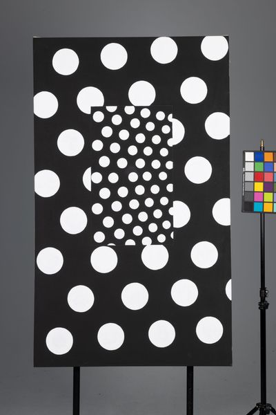 Black test chart with white circles and a color checker on a stand against a gray background