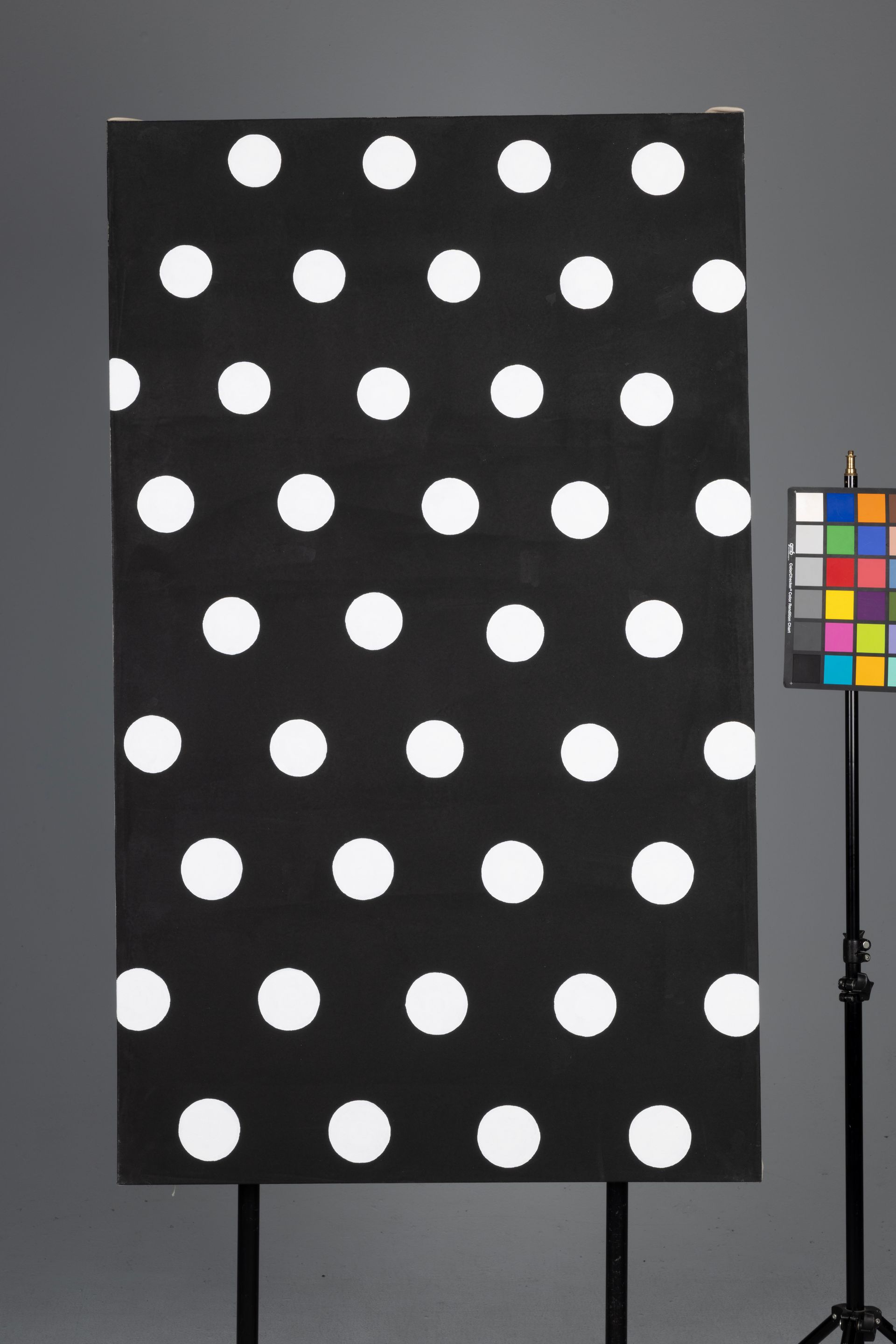 Black board with rows of white polka dots beside a color calibration chart on a stand