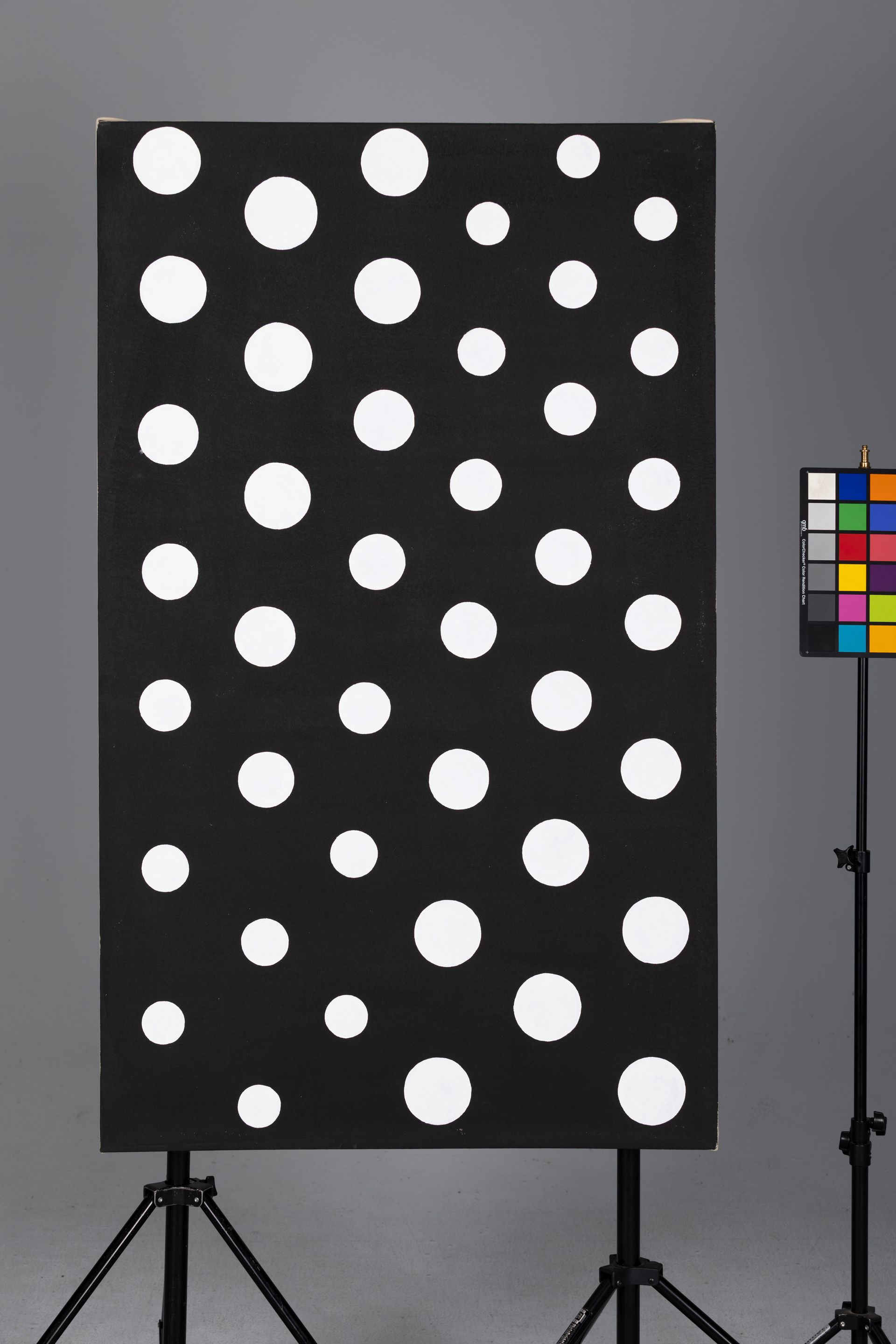 Black panel with white polka dots on a tripod stand beside a color calibration chart