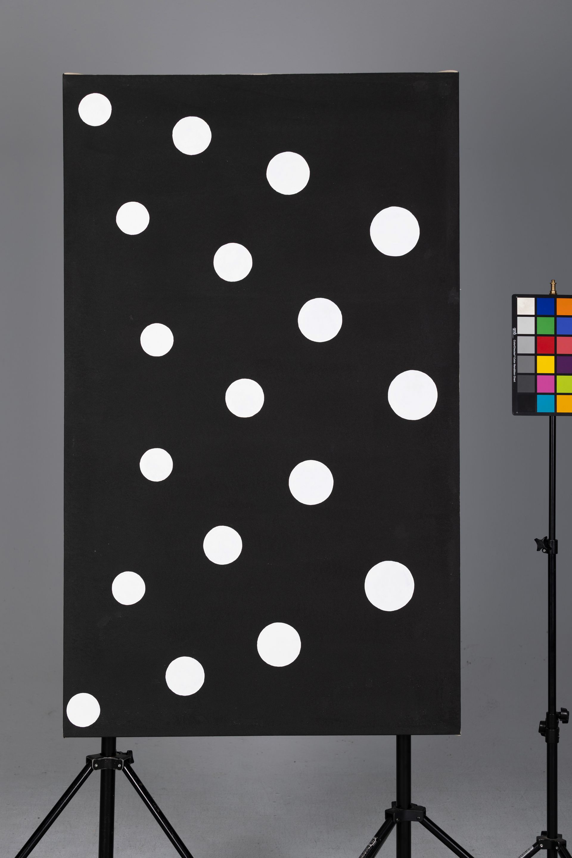 Black panel on tripod with white polka dots beside a color calibration chart