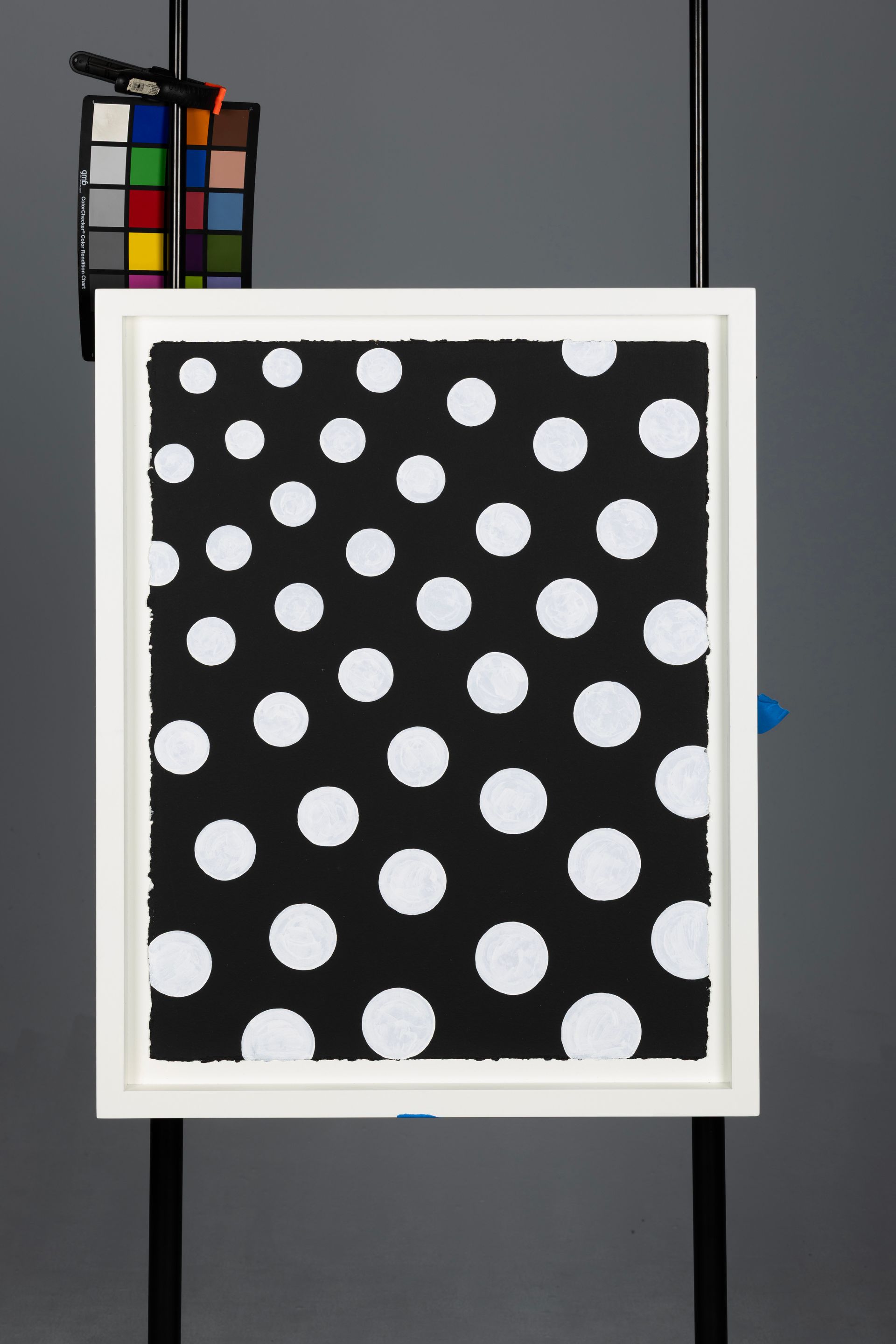 Framed black artwork with white polka dots, hanging against a gray wall.