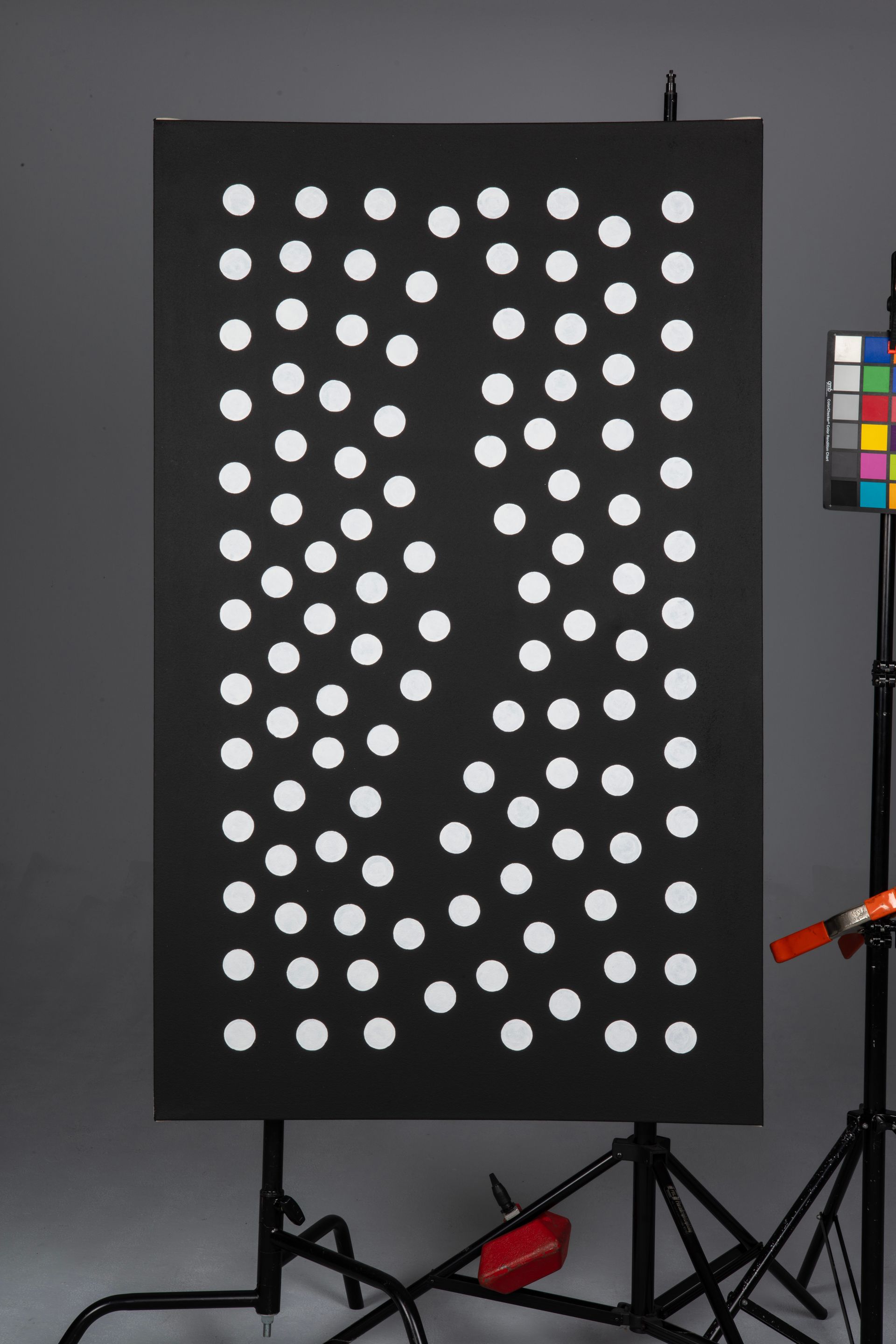 Black board with rows of white circular dots, shown in a studio setup with a color chart at the side