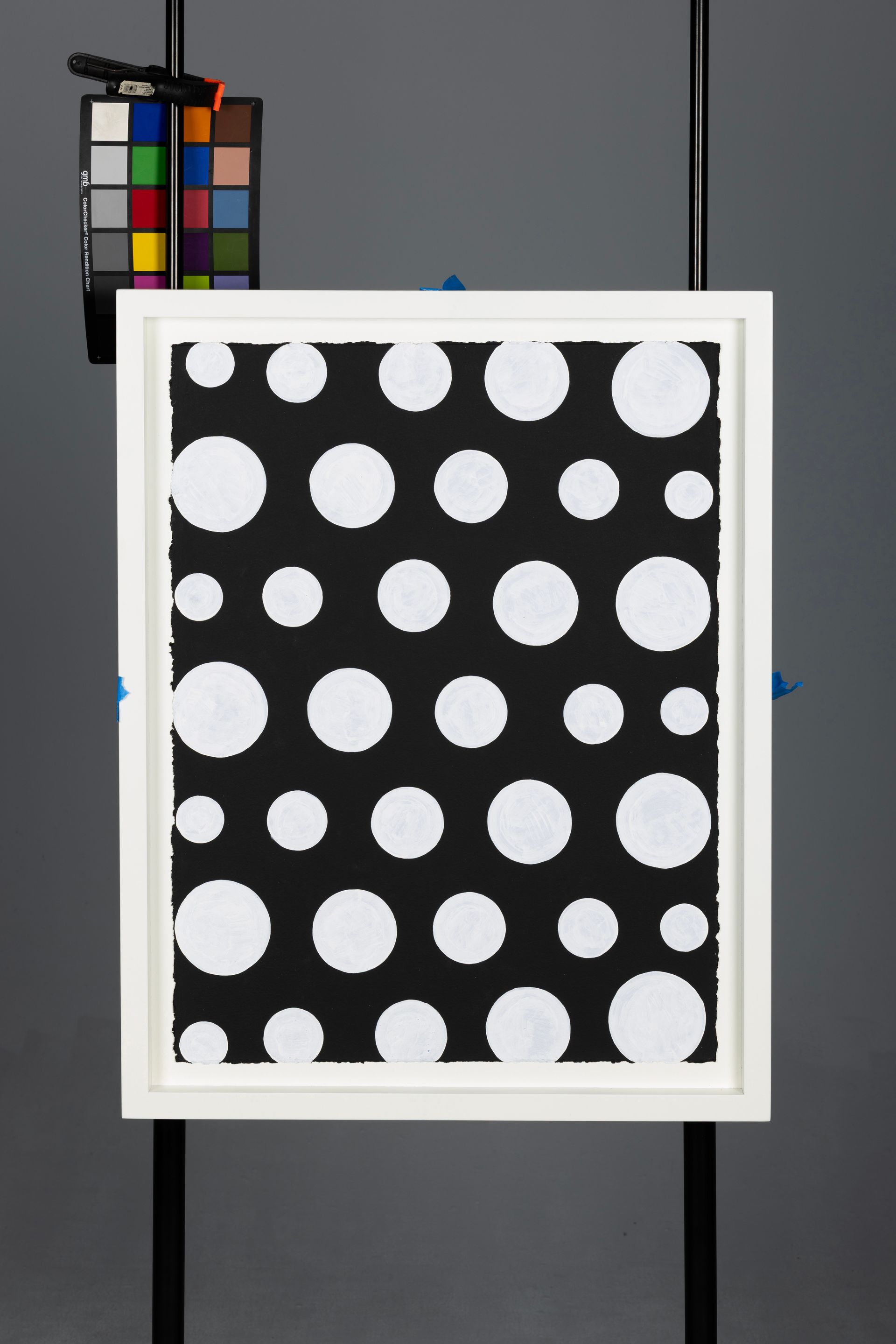 Framed black board with white polka dots, shown on a stand with a color calibration chart beside it