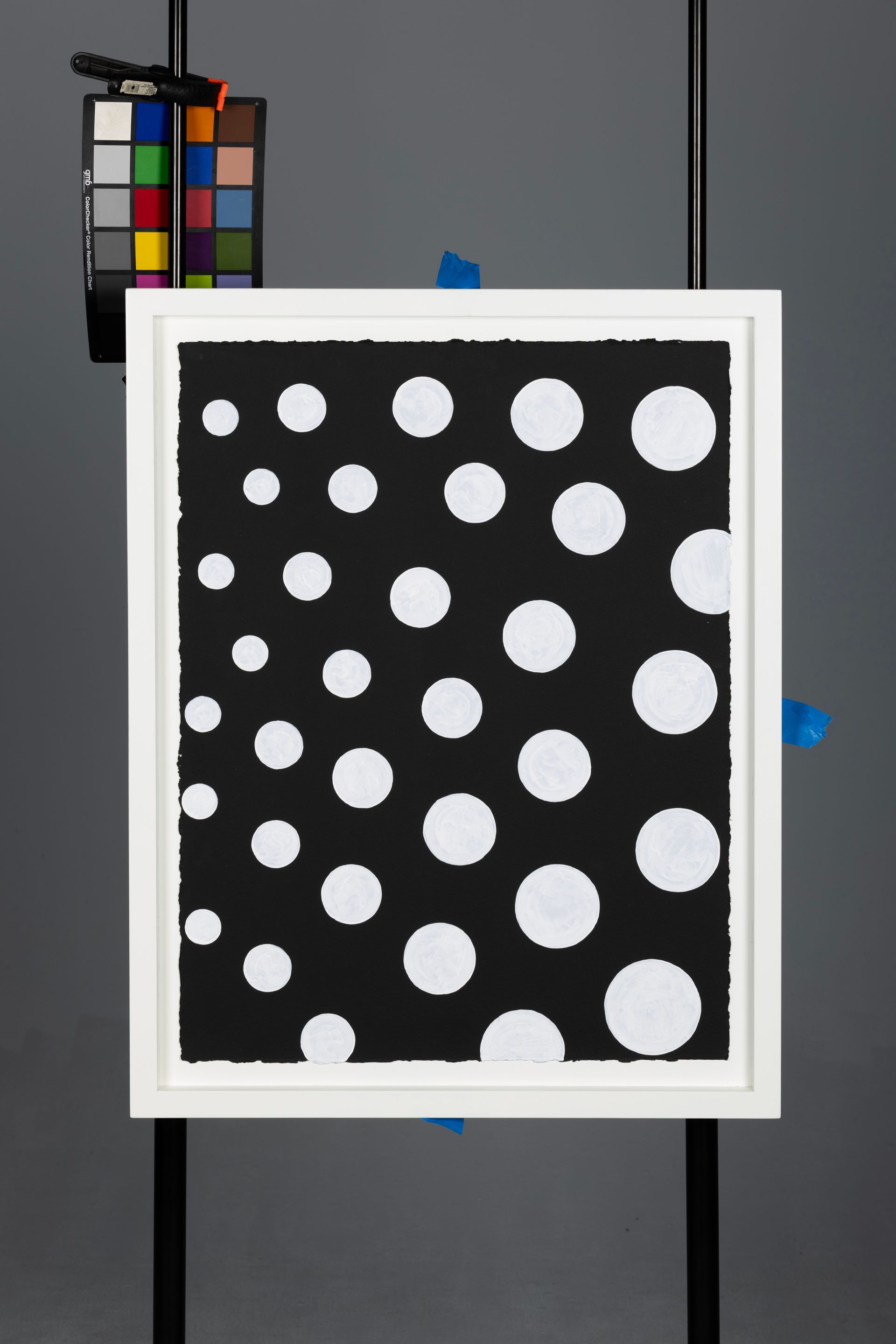 Framed black print with white polka dots on a gray background, with a color calibration chart in the corner