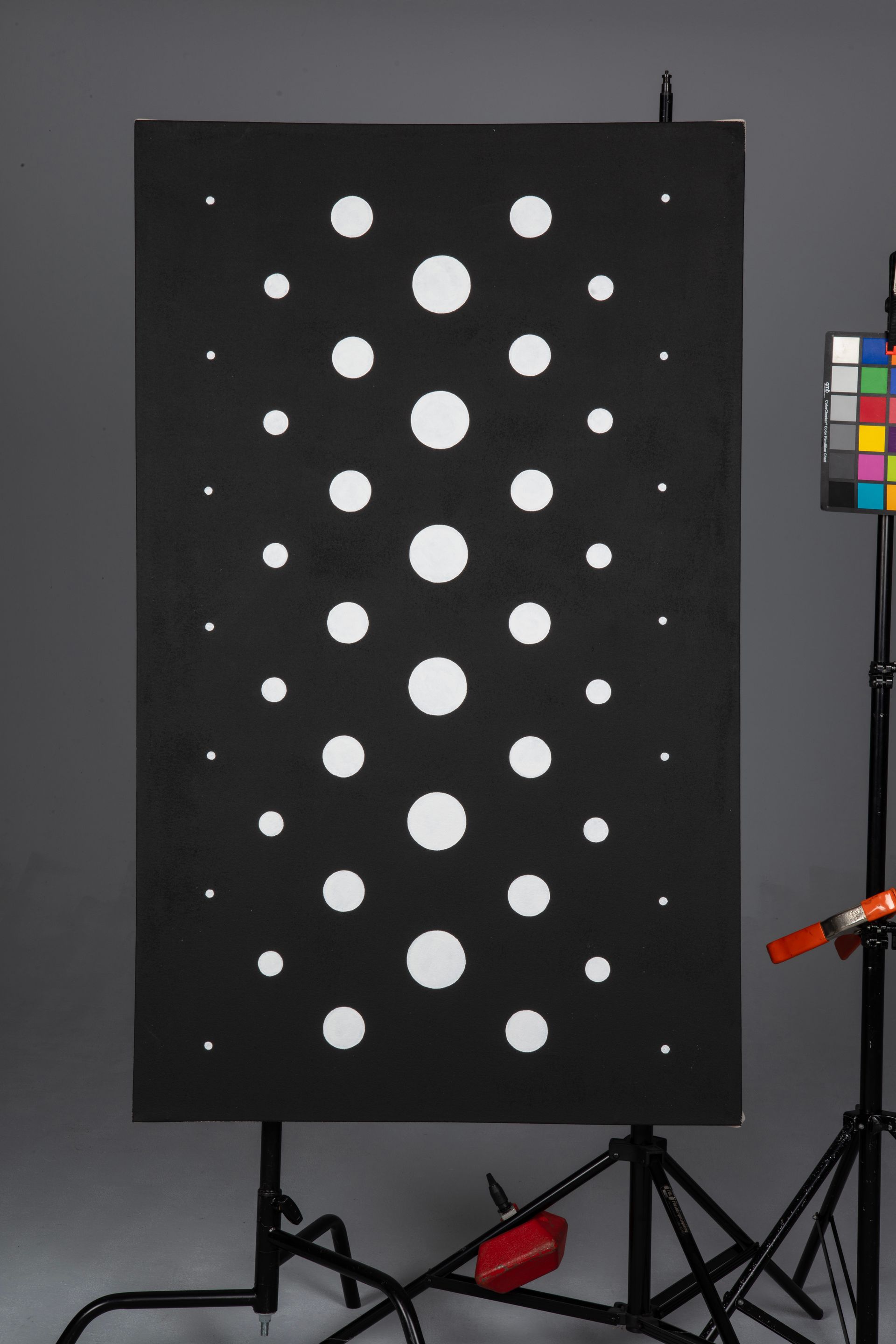 Black panel with a grid of white circular dots, shown in a studio setup with color chart and equipment.