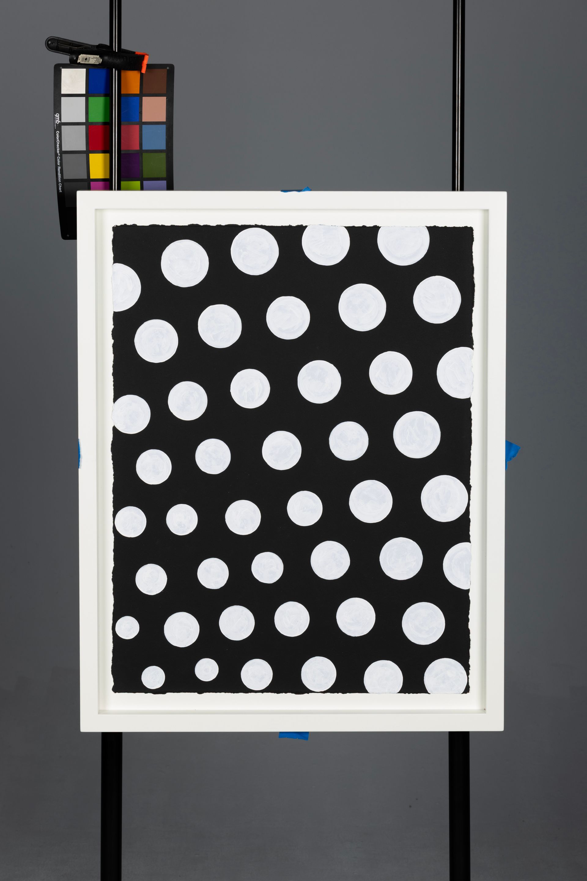 White-framed board with black background covered in white polka dots, shown with a color checker beside it.