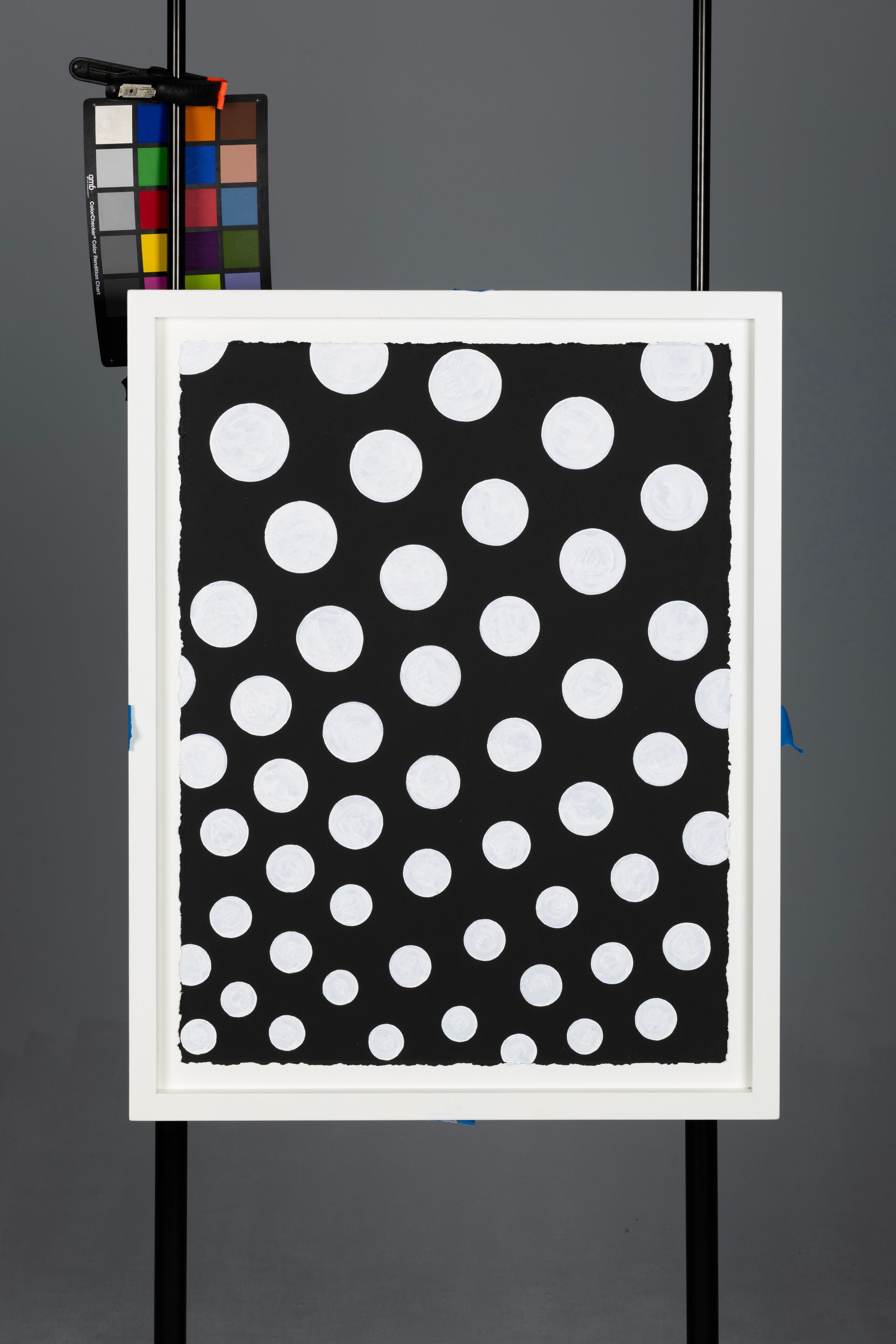 White-framed black panel with white polka dots and a color calibration chart above it