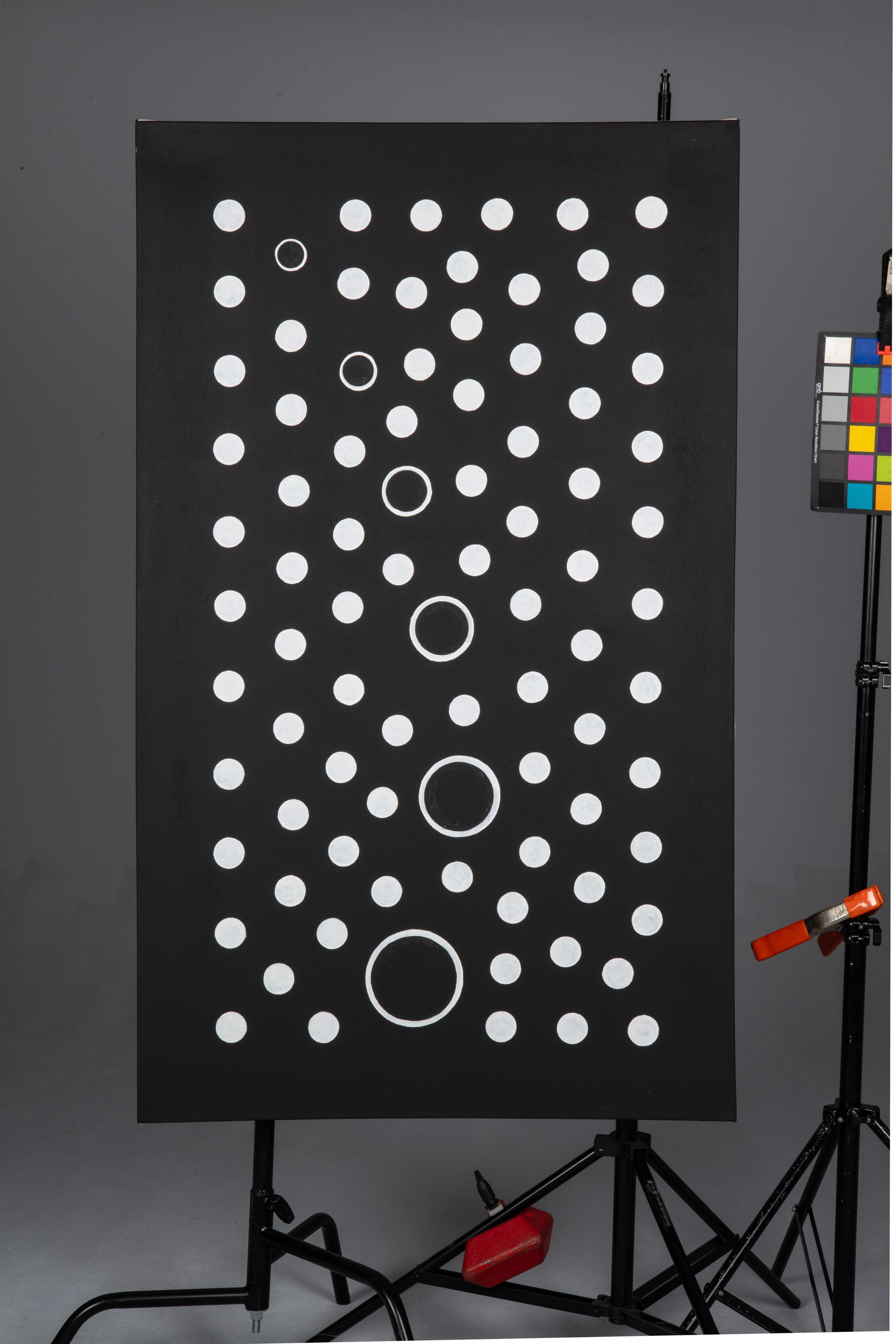 Black test board with rows of white circles and a color calibration chart on the right, on a stand.
