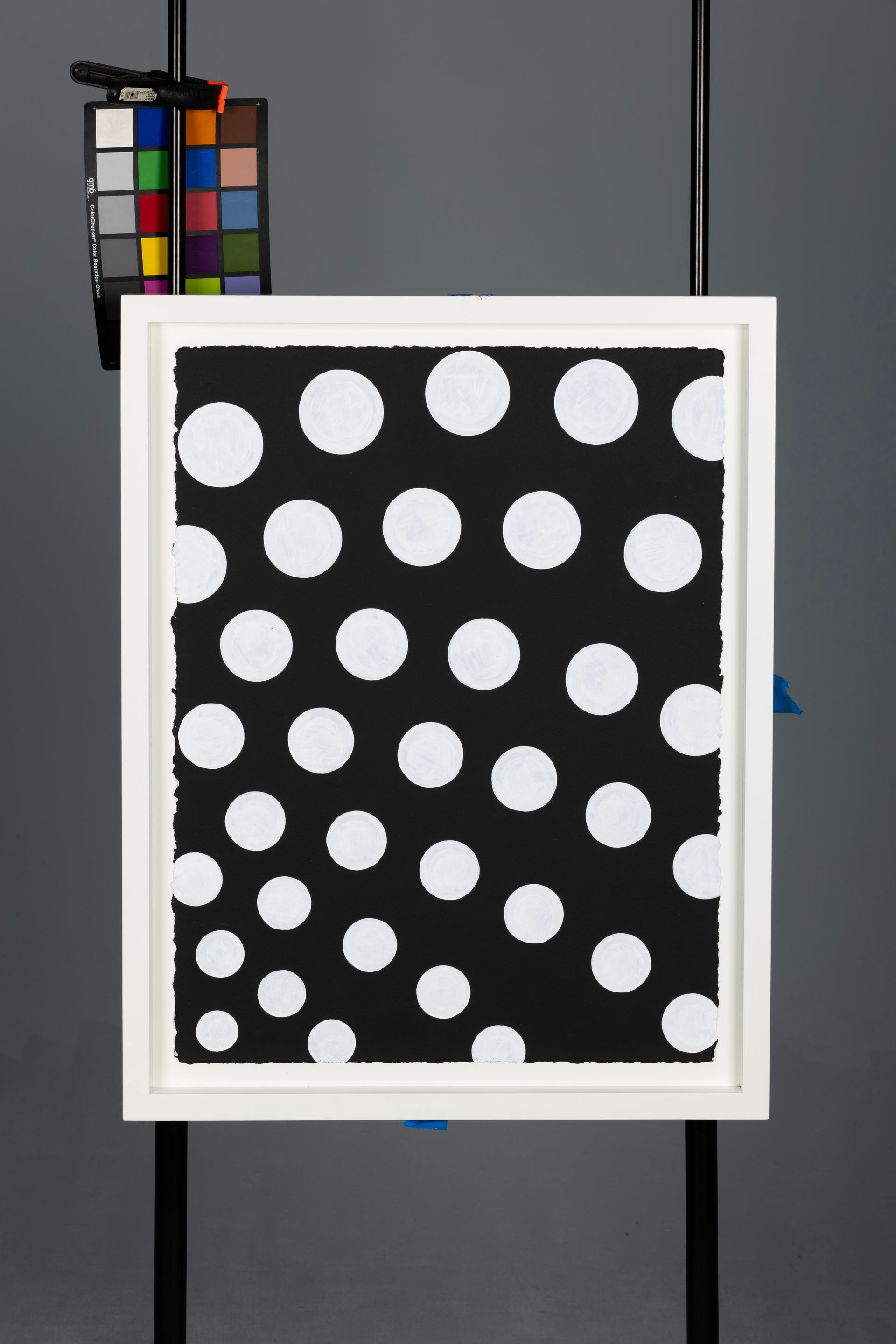 White-framed black board with scattered white polka dots, beside a color calibration chart.