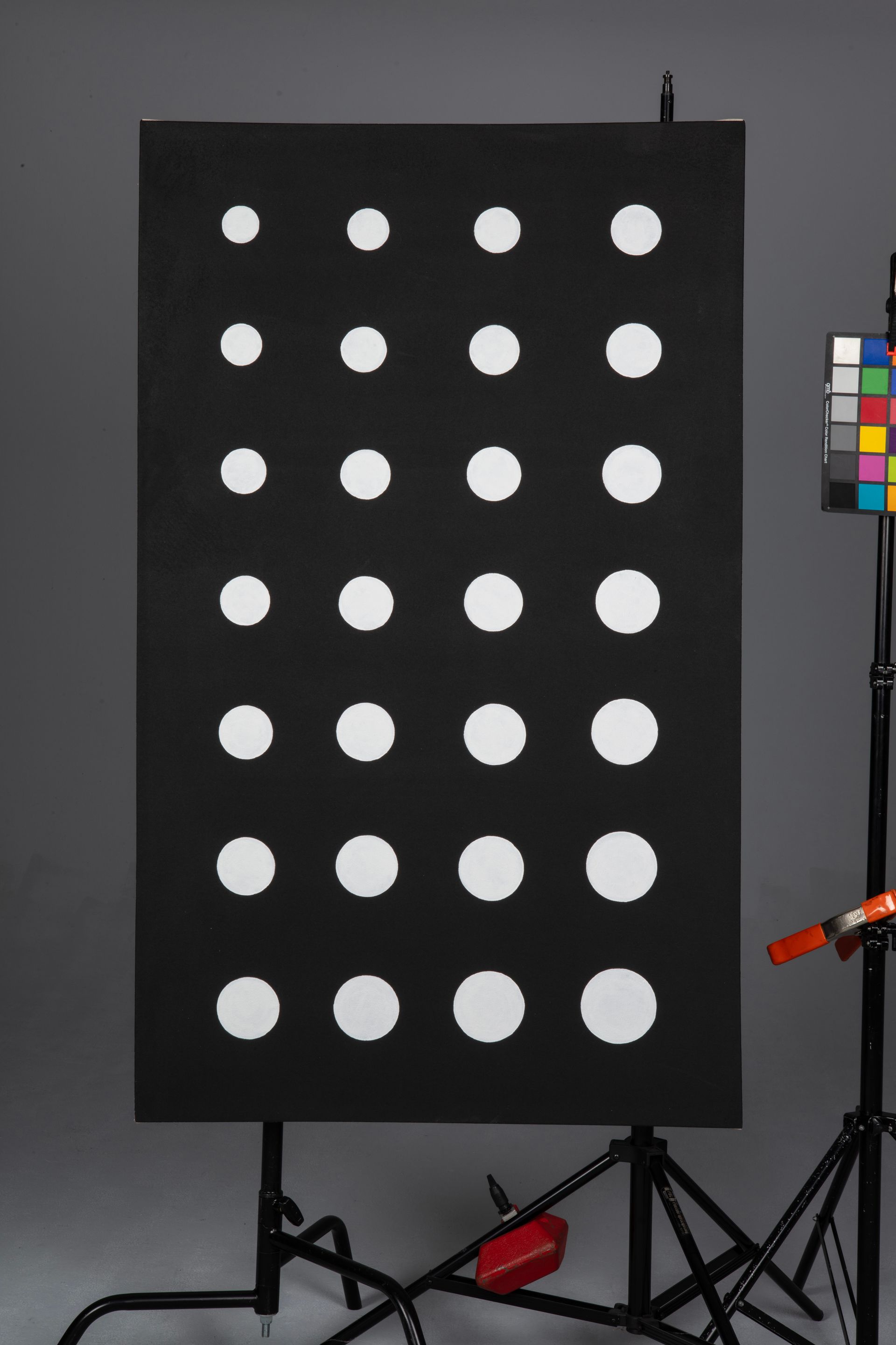 Black board with rows of white dots on a stand in a studio, with color checker and equipment visible.