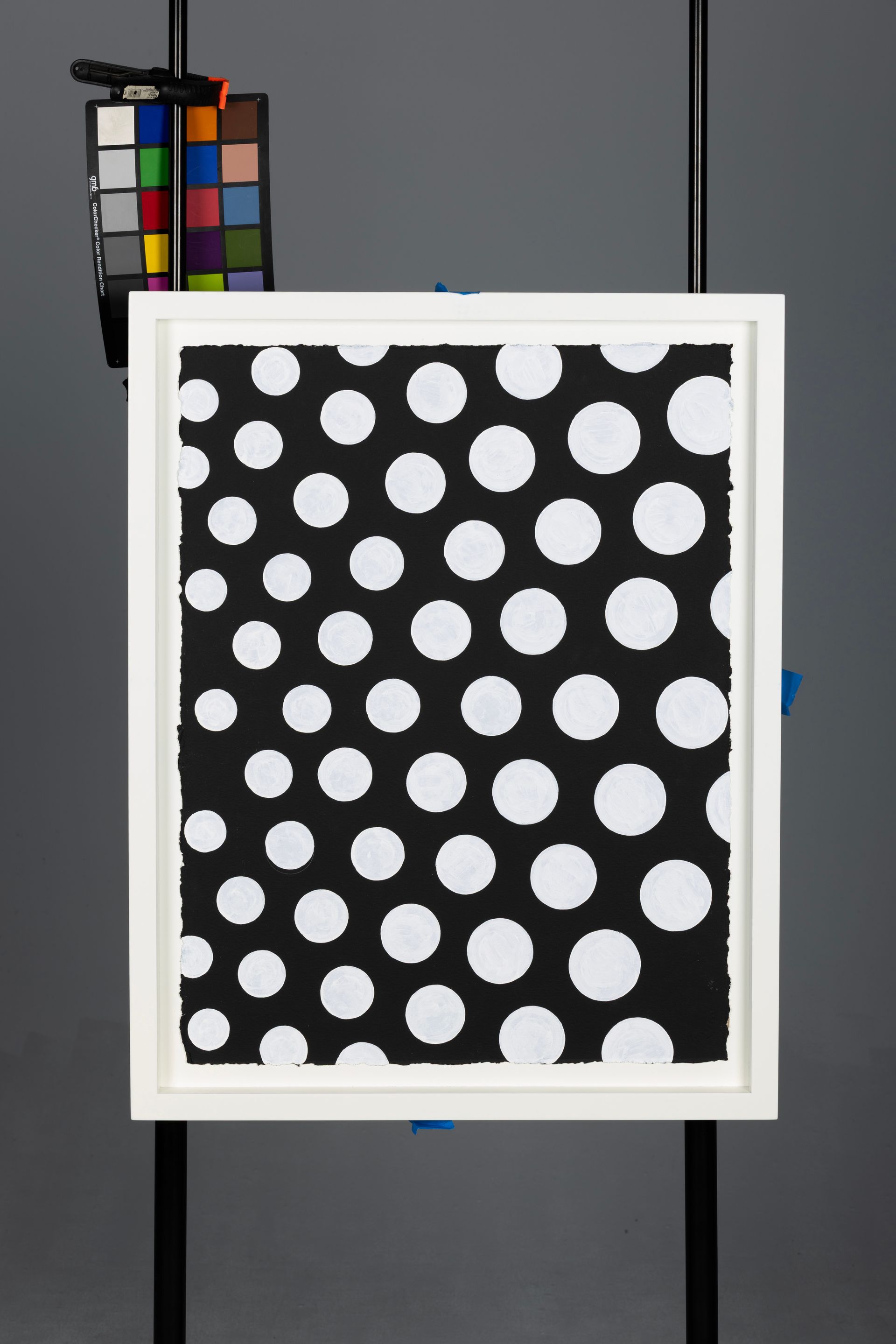Black canvas with white polka dots in a white frame, with a color calibration chart behind it
