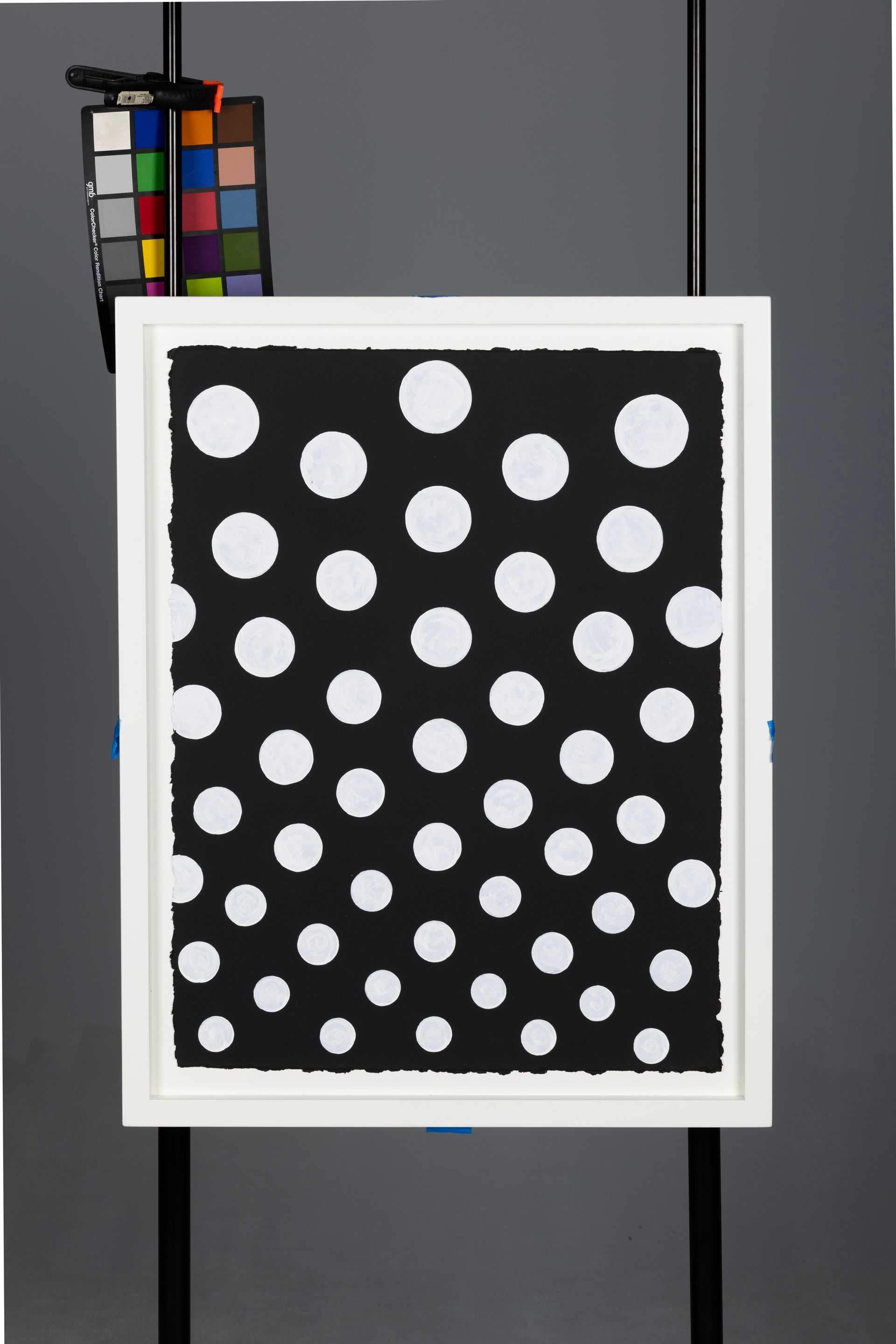 Black display board with white polka dots on a gray stand, with a color checker in the top left.